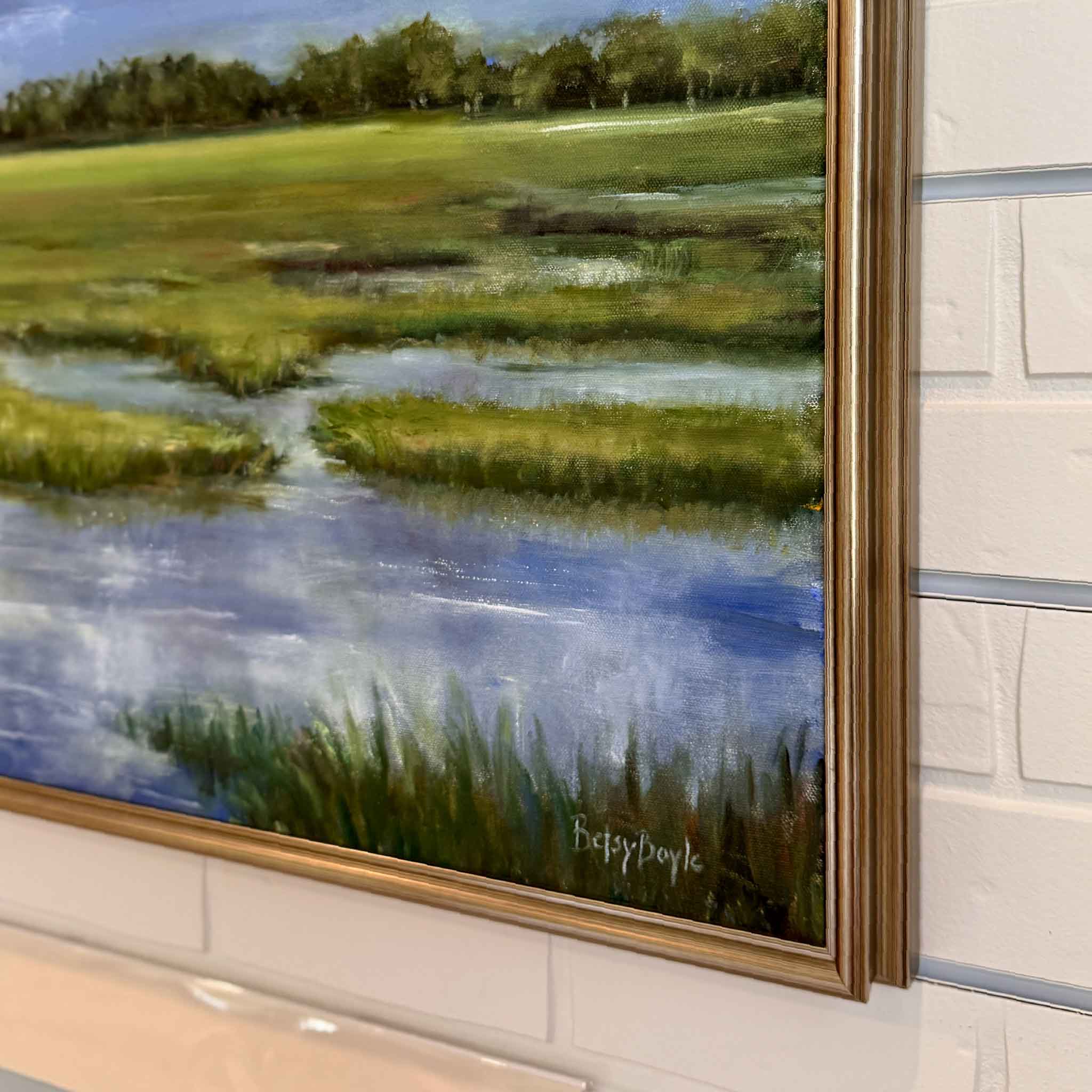 Framed oil painting of a serene Lowcountry marsh landscape under a dramatic sky filled with billowing white clouds. The scene features lush green grasses, reflective tidal pools, and a distant tree line, all set against a vibrant blue sky.