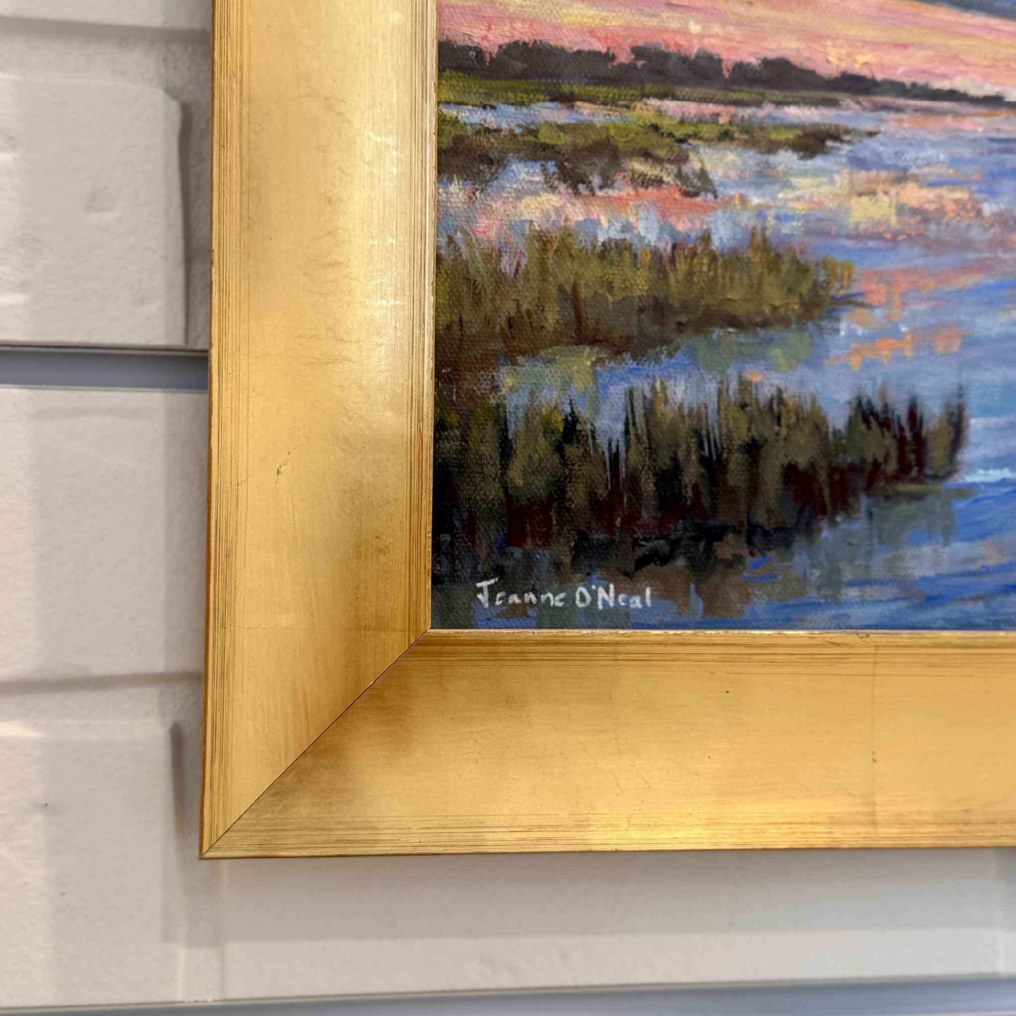 Framed painting of a landscape low country marsh with water and sky on a white brick wall