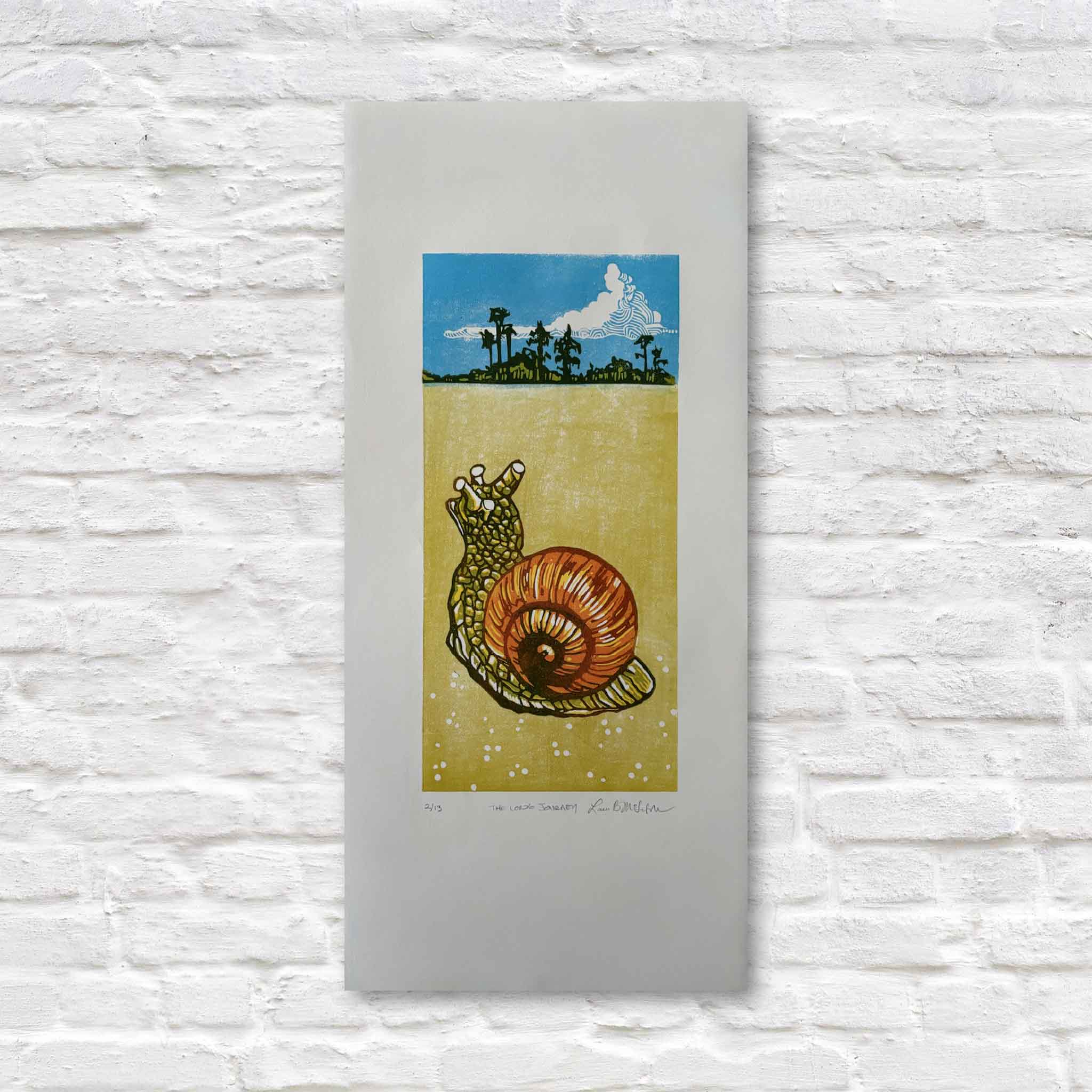 linocut artwork of a snail on soft white paper, displayed on a textured white wall.