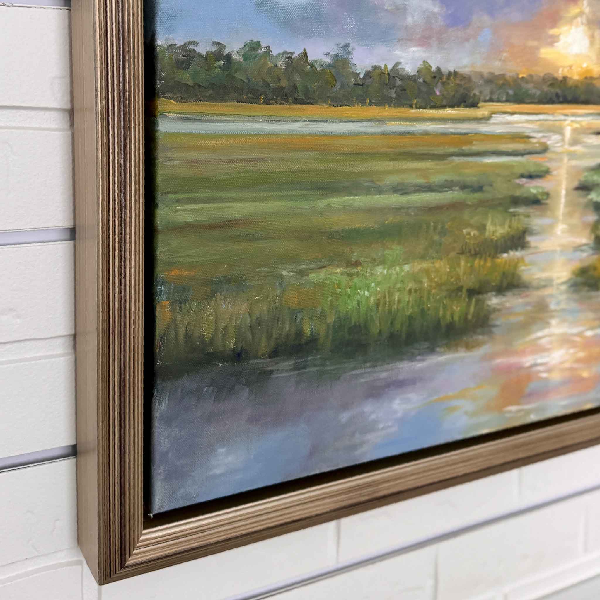 Framed oil painting of a vibrant Lowcountry sunset over a marsh. Bold clouds streak across the sky in shades of blue, lavender, and gray, opening to reveal a glowing orange sun at the horizon. The sunlight reflects down a winding tidal creek, bordered by lush green grasses, with a distant tree line and a lone white bird in flight.