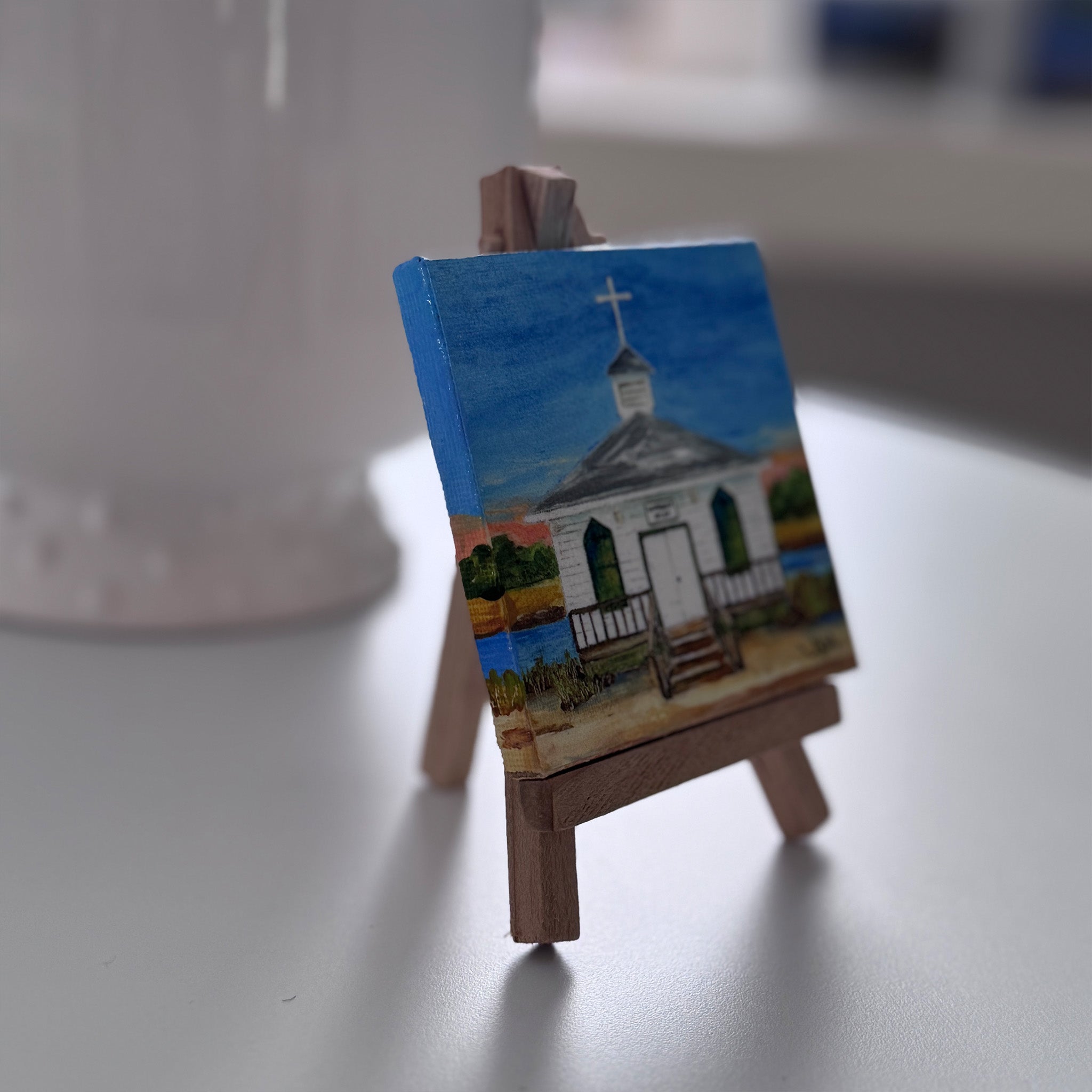Small painting of a church on a wooden easel with a blurred background
