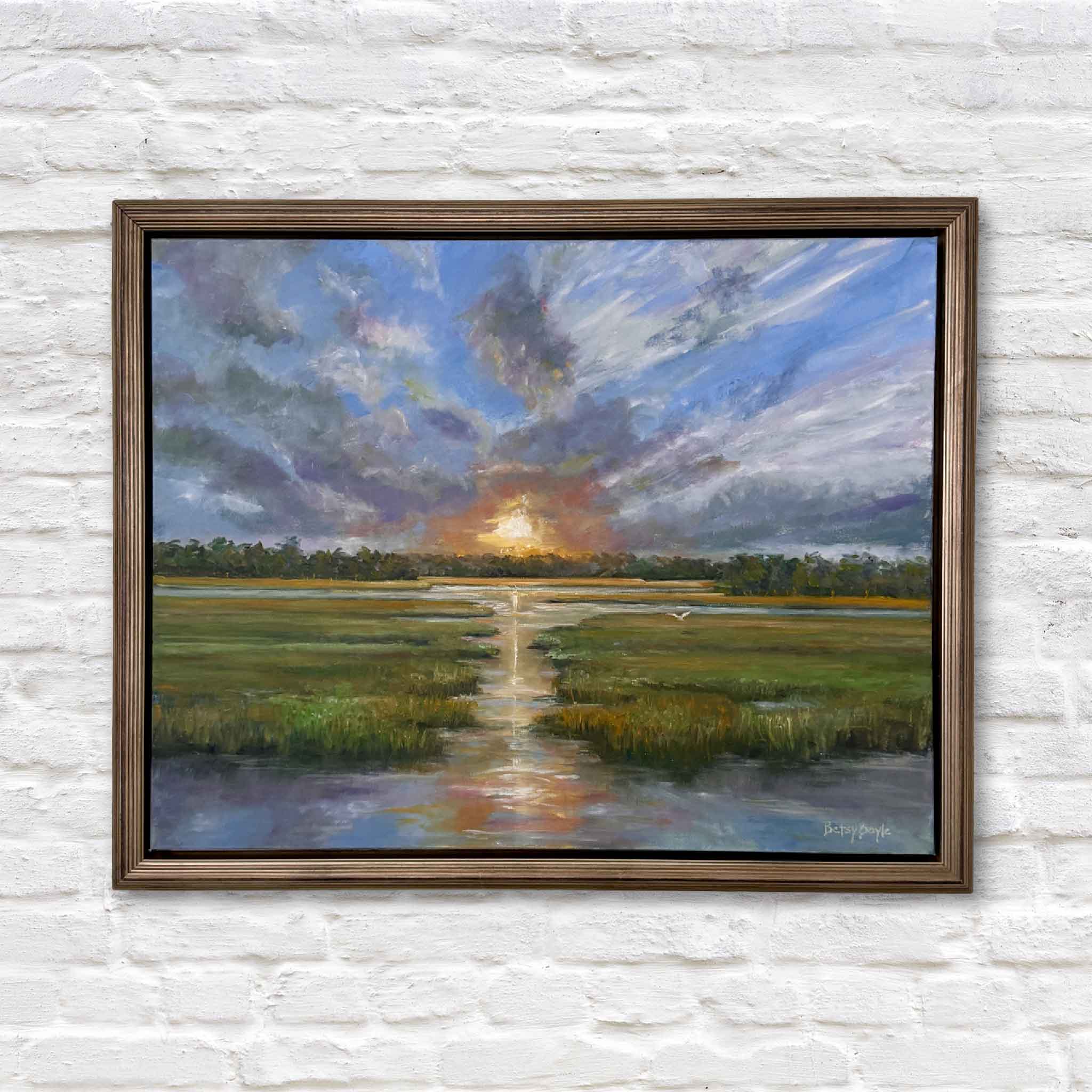 Framed oil painting of a vibrant Lowcountry sunset over a marsh. Bold clouds streak across the sky in shades of blue, lavender, and gray, opening to reveal a glowing orange sun at the horizon. The sunlight reflects down a winding tidal creek, bordered by lush green grasses, with a distant tree line and a lone white bird in flight.