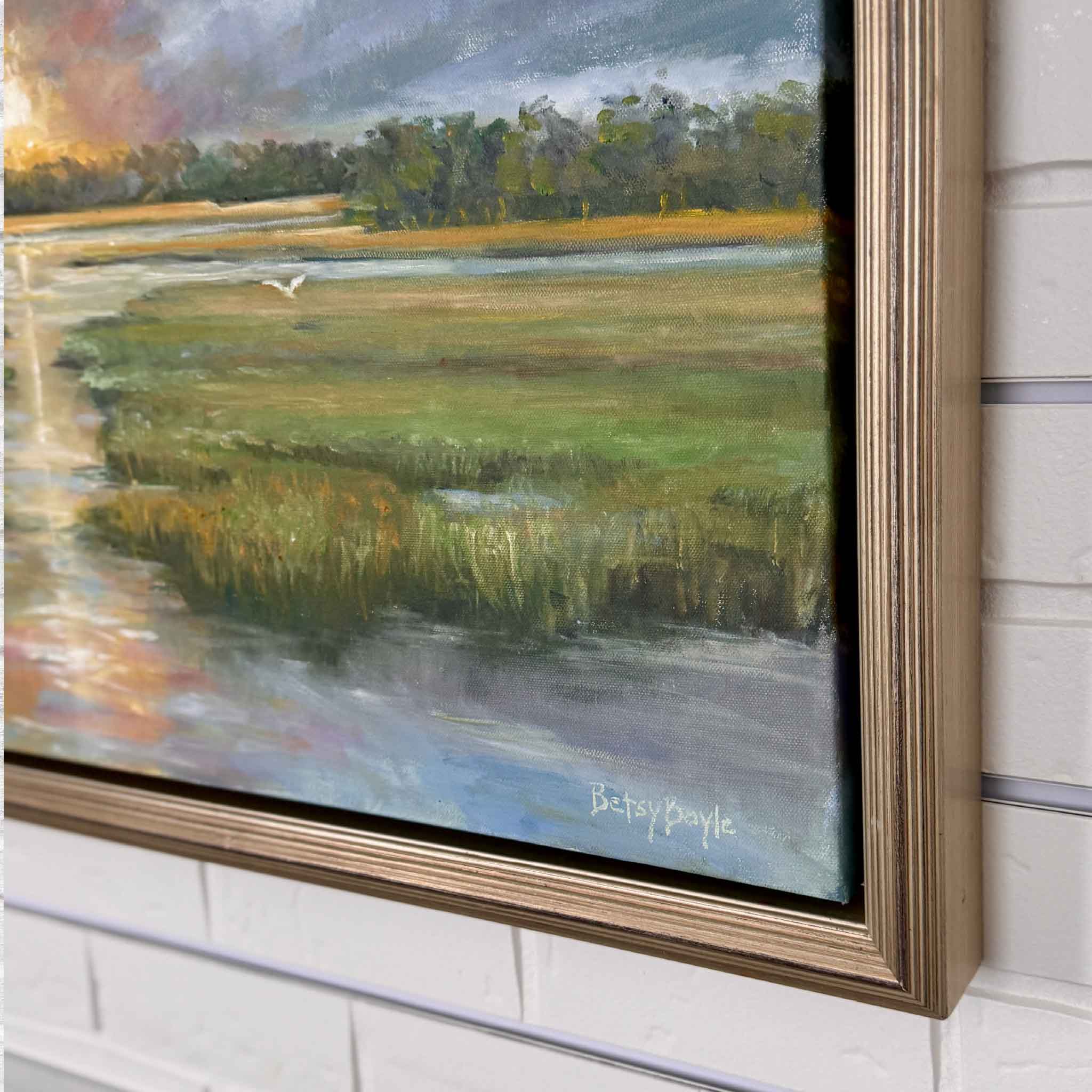 Framed oil painting of a vibrant Lowcountry sunset over a marsh. Bold clouds streak across the sky in shades of blue, lavender, and gray, opening to reveal a glowing orange sun at the horizon. The sunlight reflects down a winding tidal creek, bordered by lush green grasses, with a distant tree line and a lone white bird in flight.