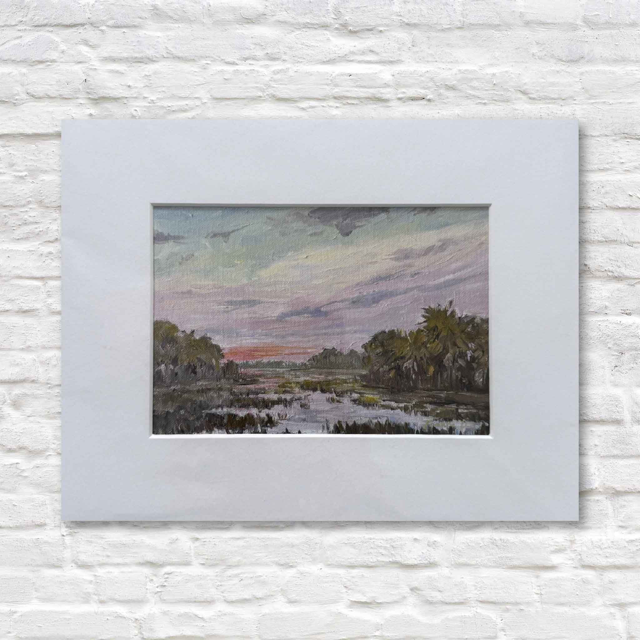 matted painting of a landscape with trees and sky on a white brick wall.