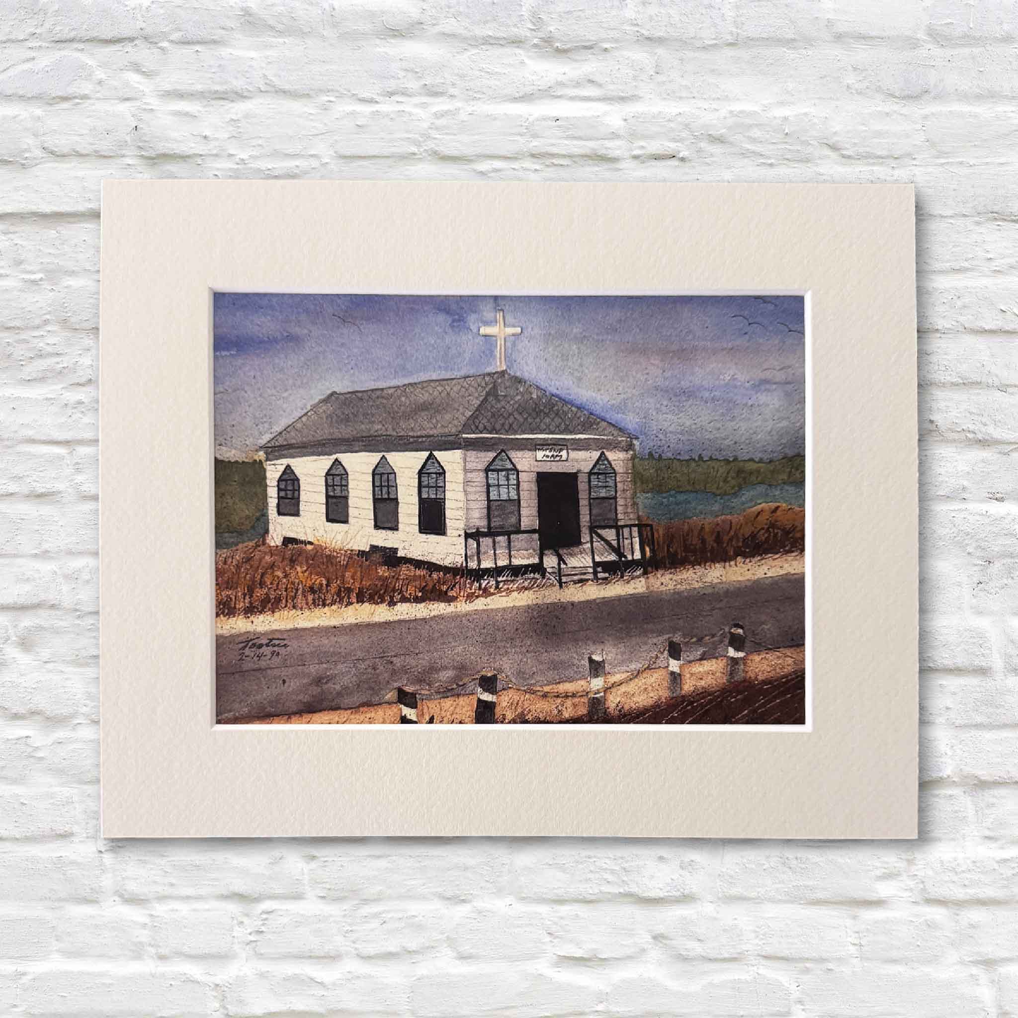 Art print of a small church by a body of water on a textured white wall.