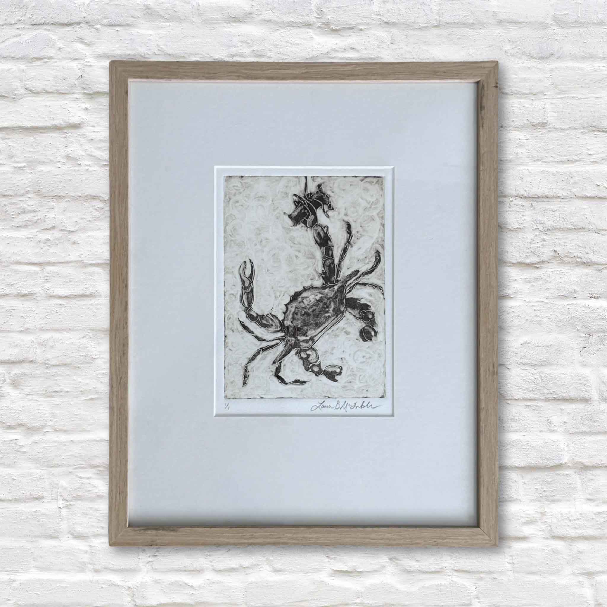 Framed artwork of a crab on a light blue background, mounted on a textured white wall.