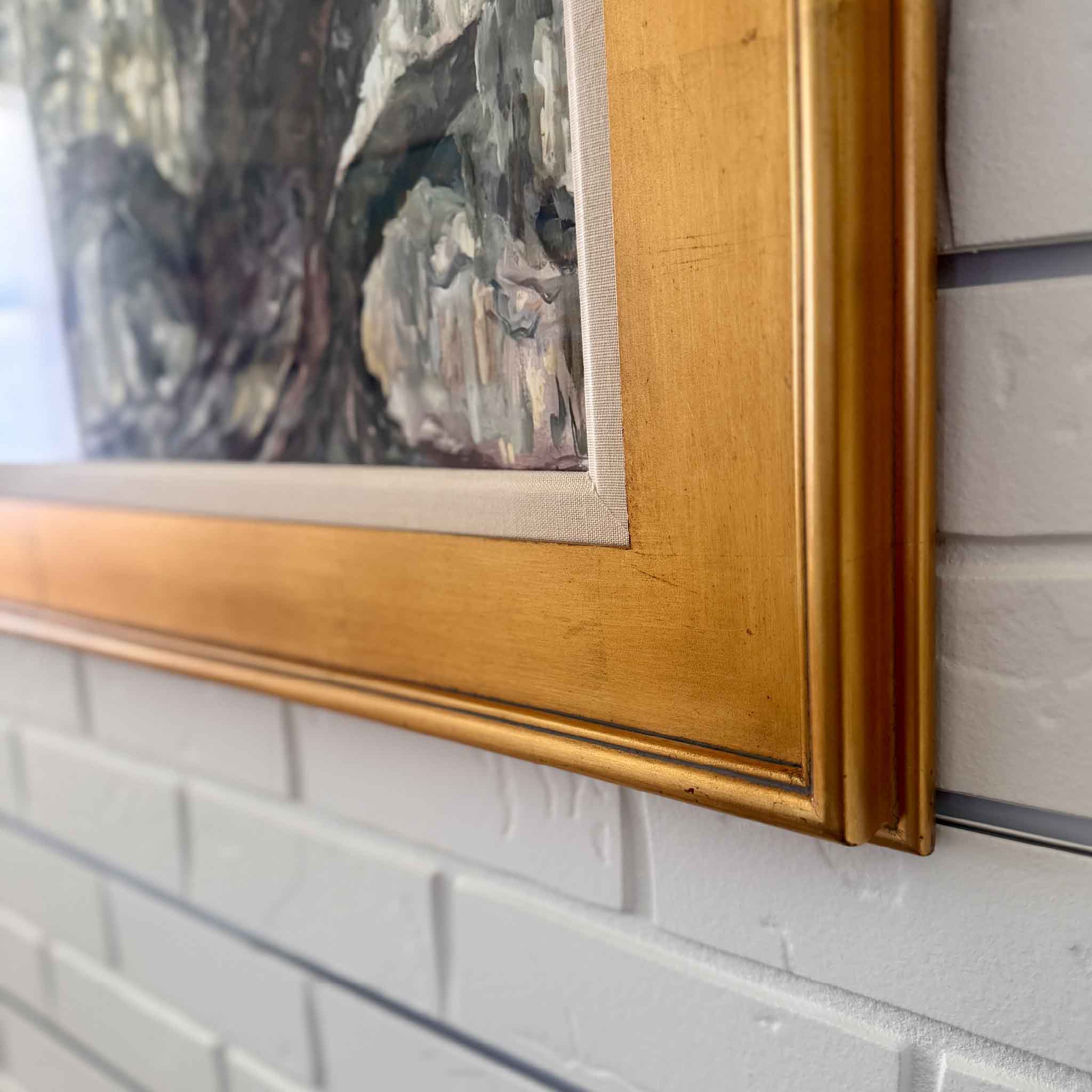 Gold-framed painting on a white brick wall