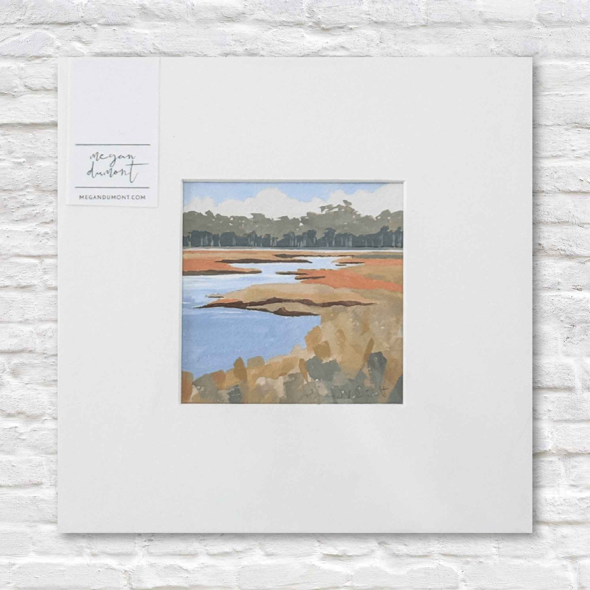 matted artwork of a coastal landscape with marsh and trees  in the background on a white brick wall.