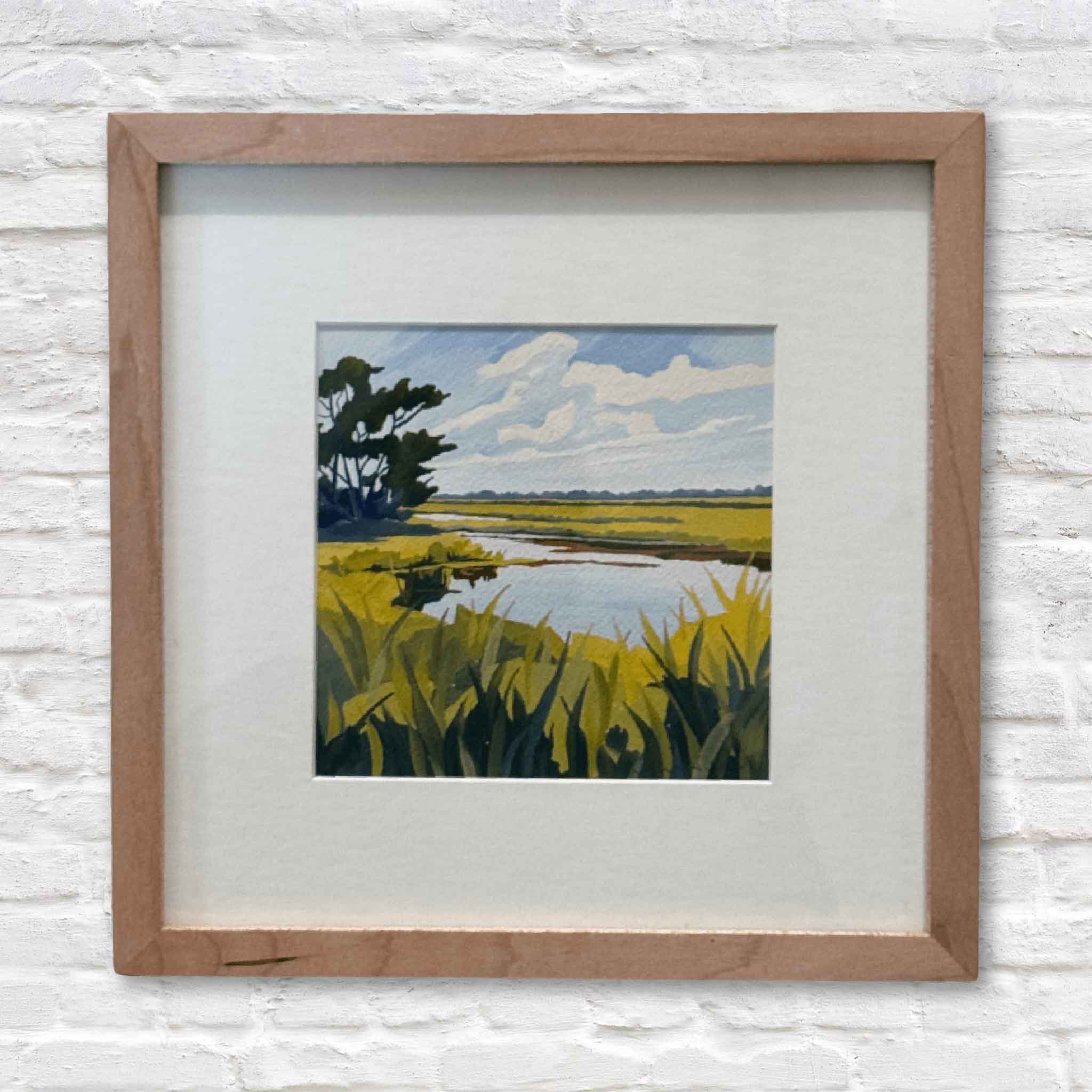 Framed artwork of a landscape with trees, water, and grass on a white brick wall.