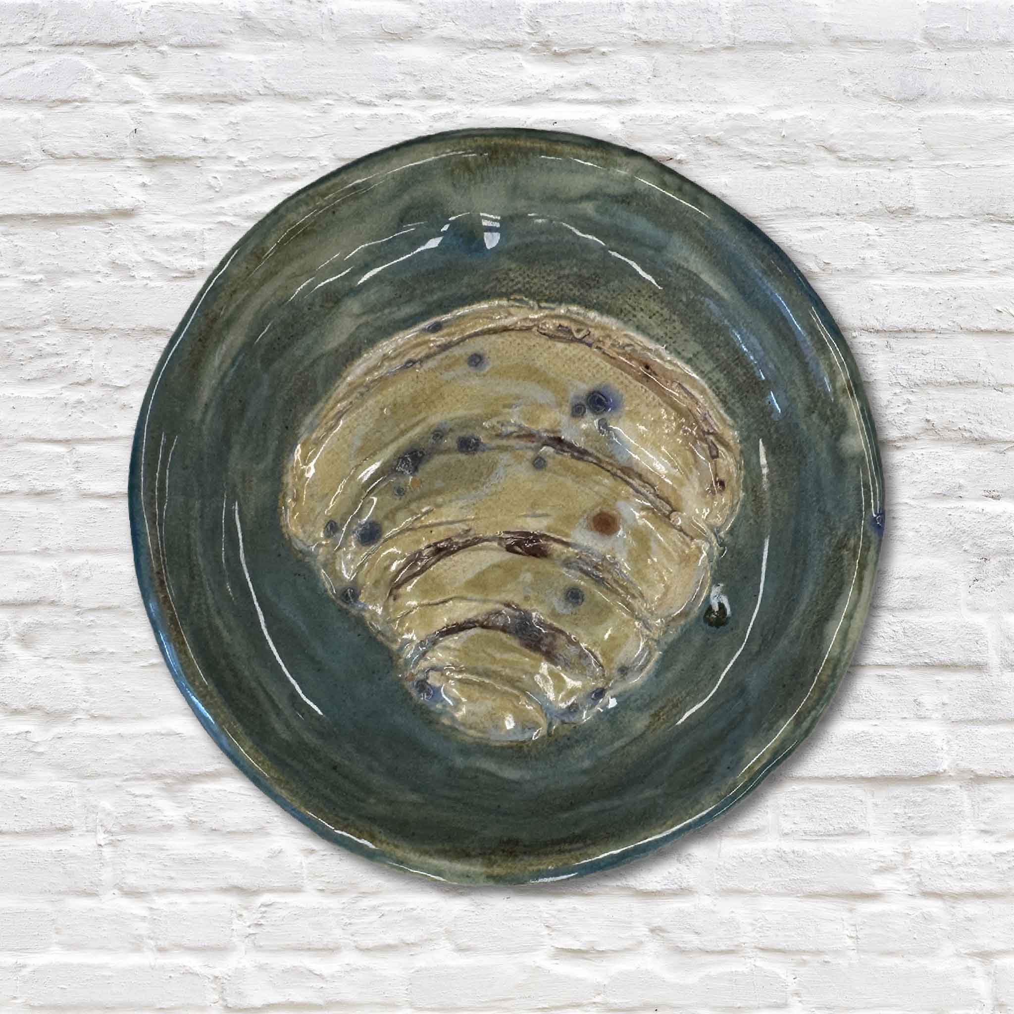 green pottery dish with pawleys island shell design on white brick wall
