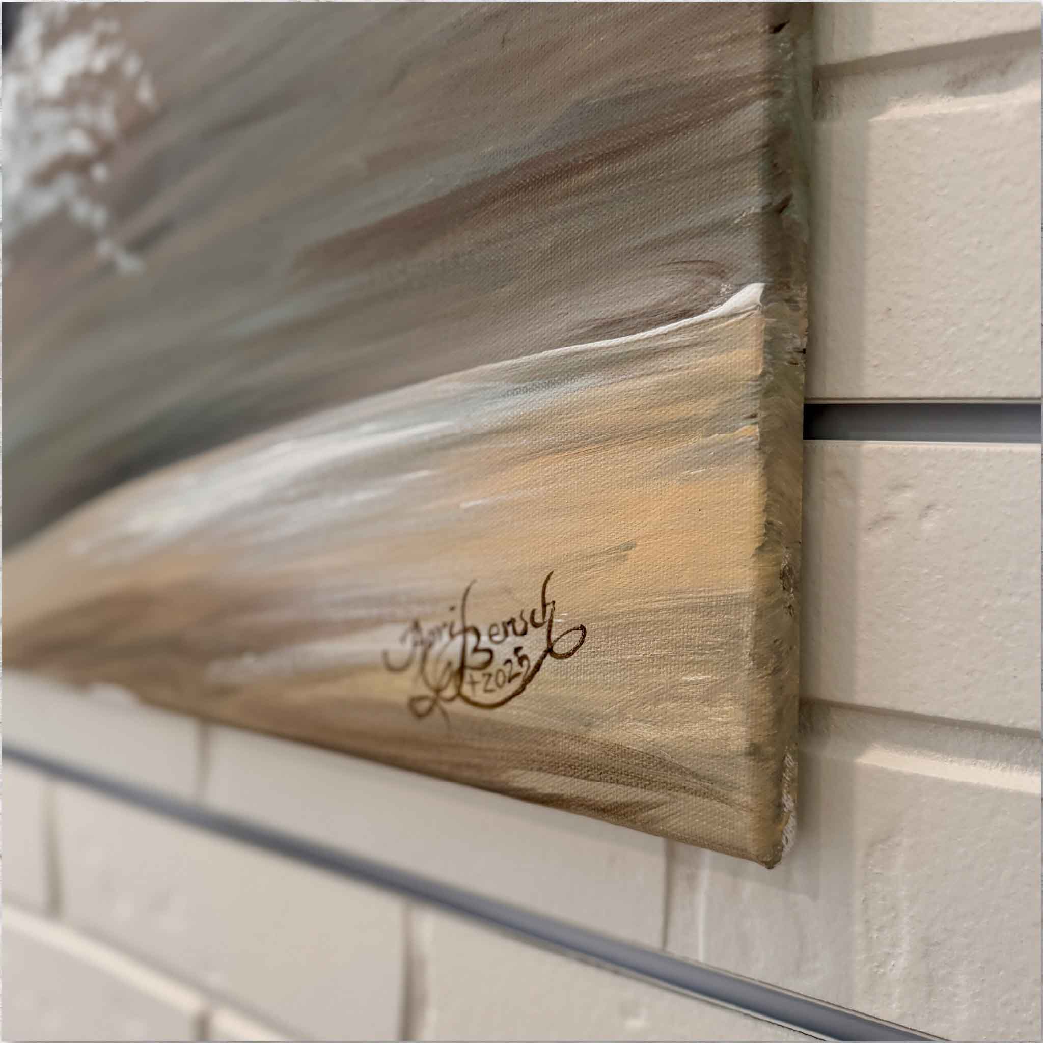 Artist signature on an original painting against a white brick wall