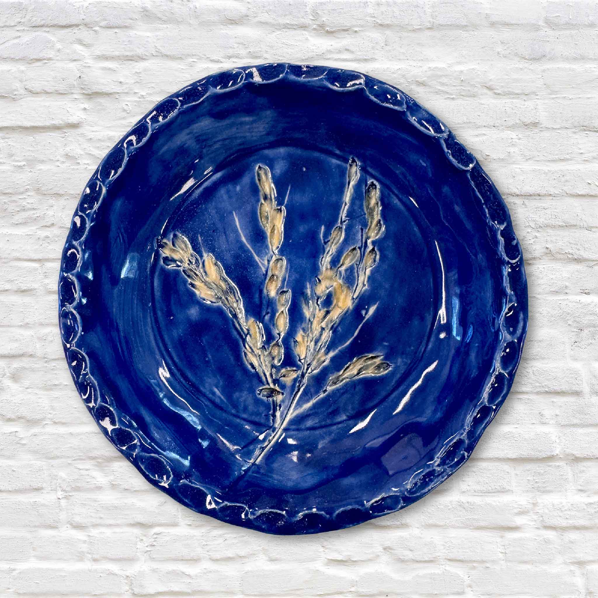indigo blue pottery plate with gold rice design in center on white brick wall
