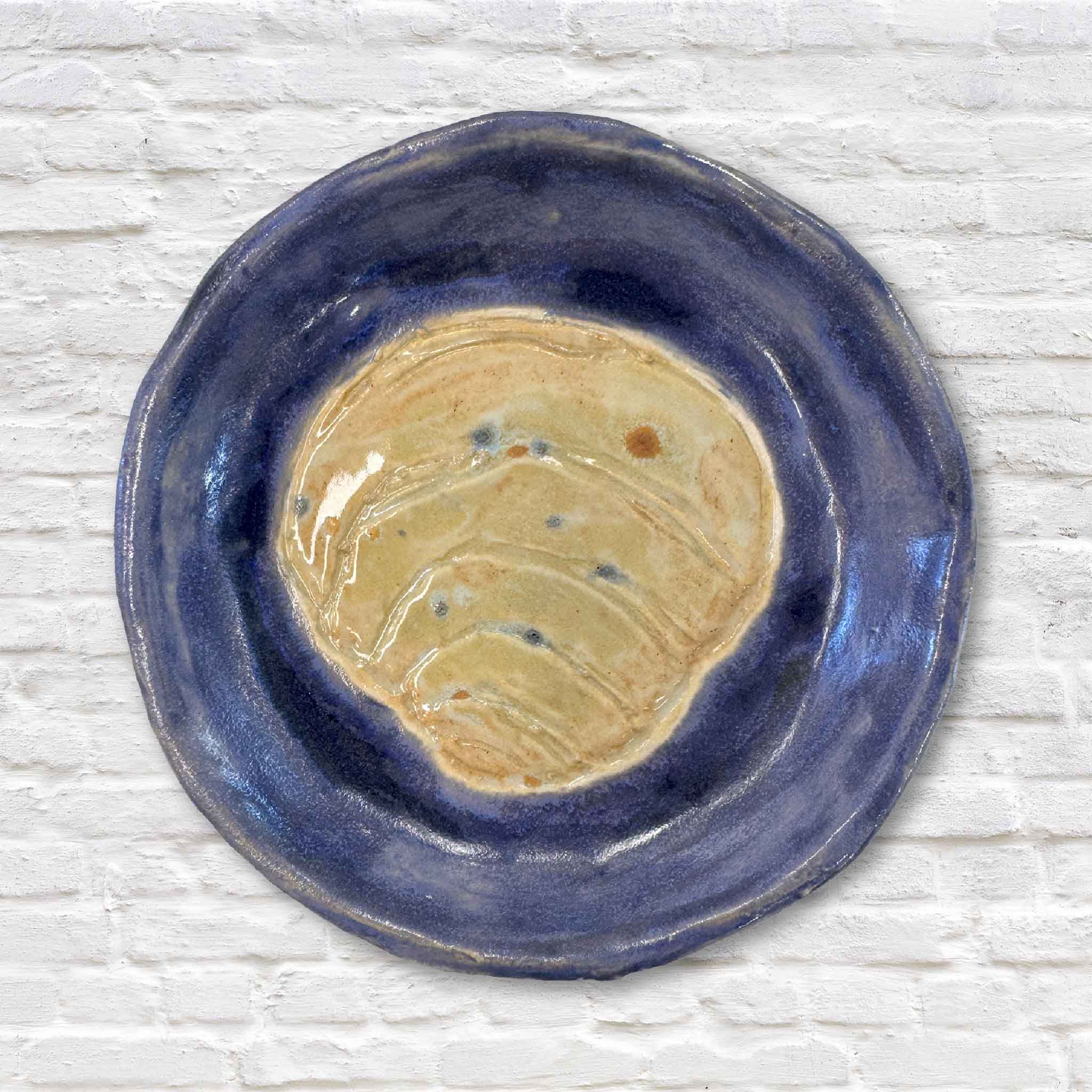 blue pottery dish with pawleys island shell in center on white brick wall