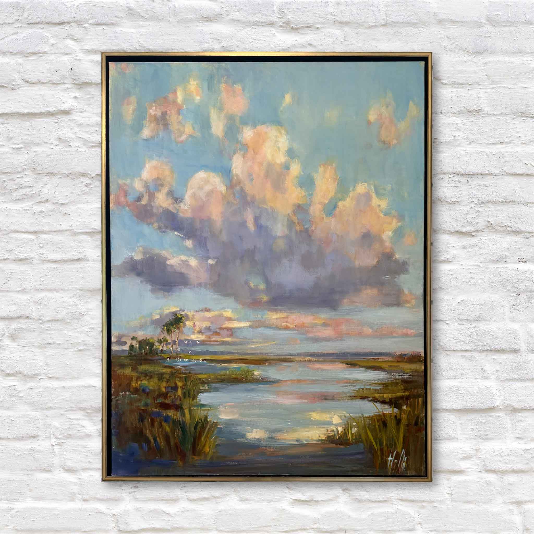 Framed oil painting of a sunset over a lowcountry marsh hanging on a white brick wall
