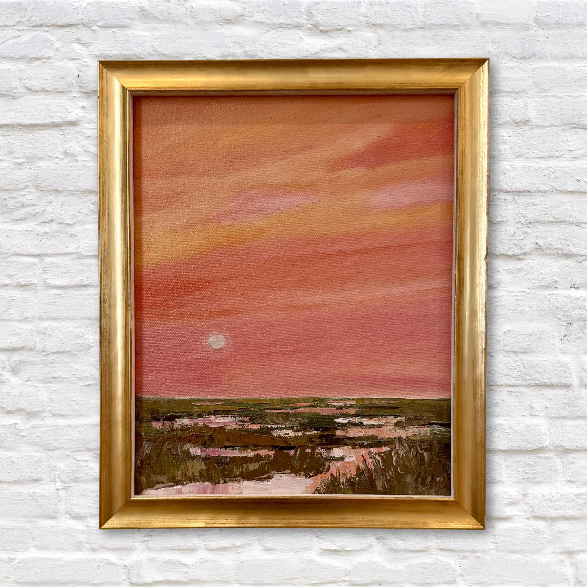 Gold framed oil painting of a sunset over lowcountry marsh a white brick wall