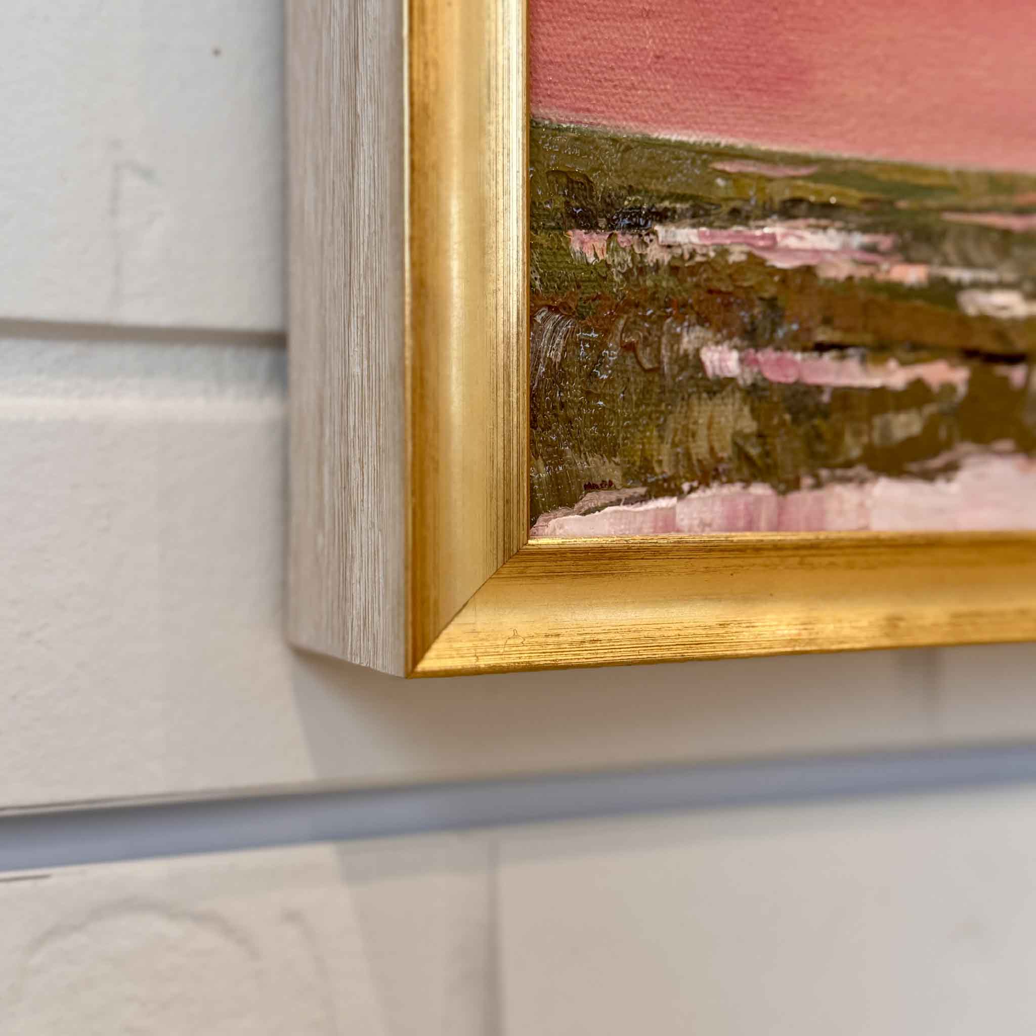 Gold framed oil painting of a sunset over lowcountry marsh a white brick wall
