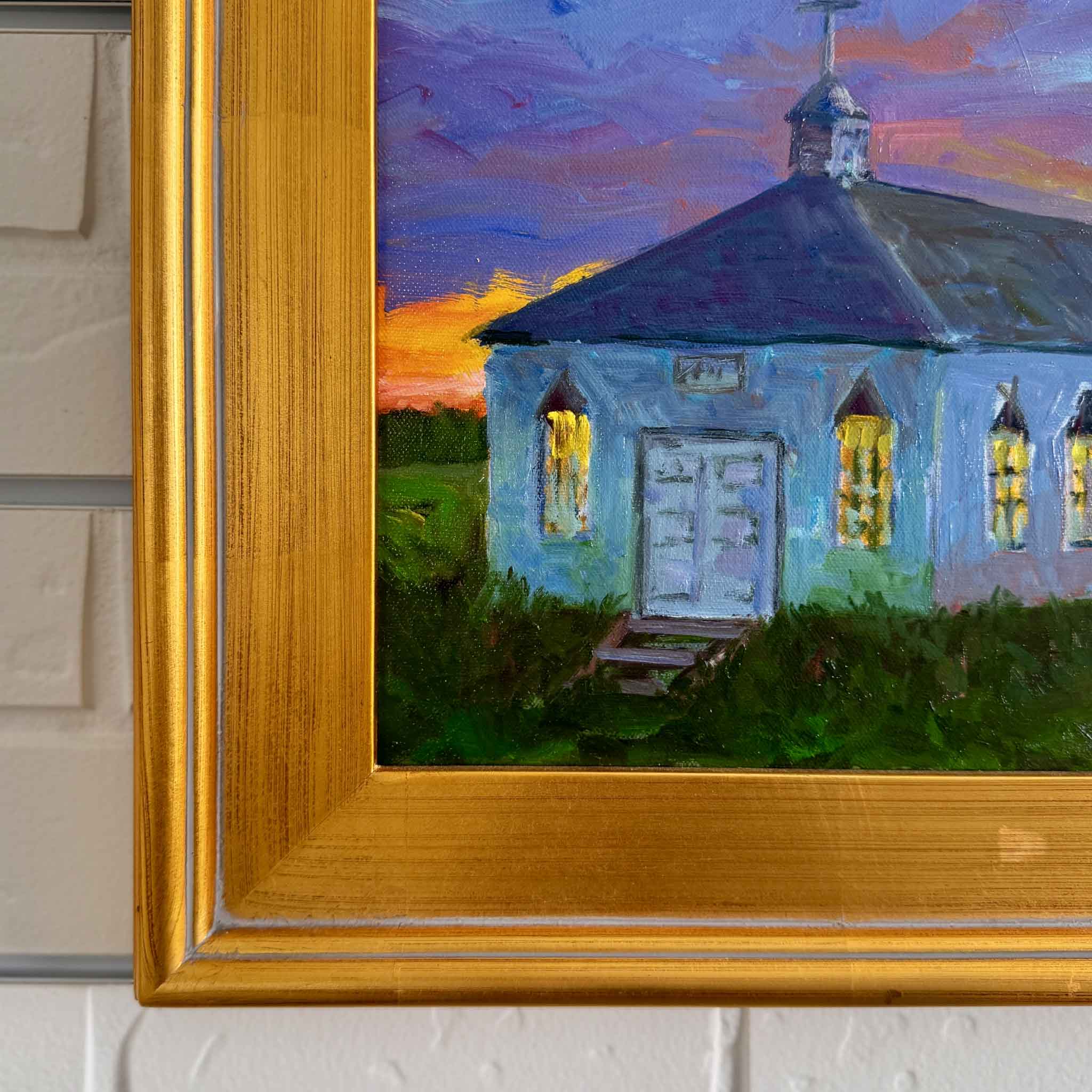 Oil painting of Pawleys Island Chapel at sunset by local artist Kathy Robinson, framed in gold. The white chapel glows against a dramatic Lowcountry sky with vivid orange, purple, and blue tones