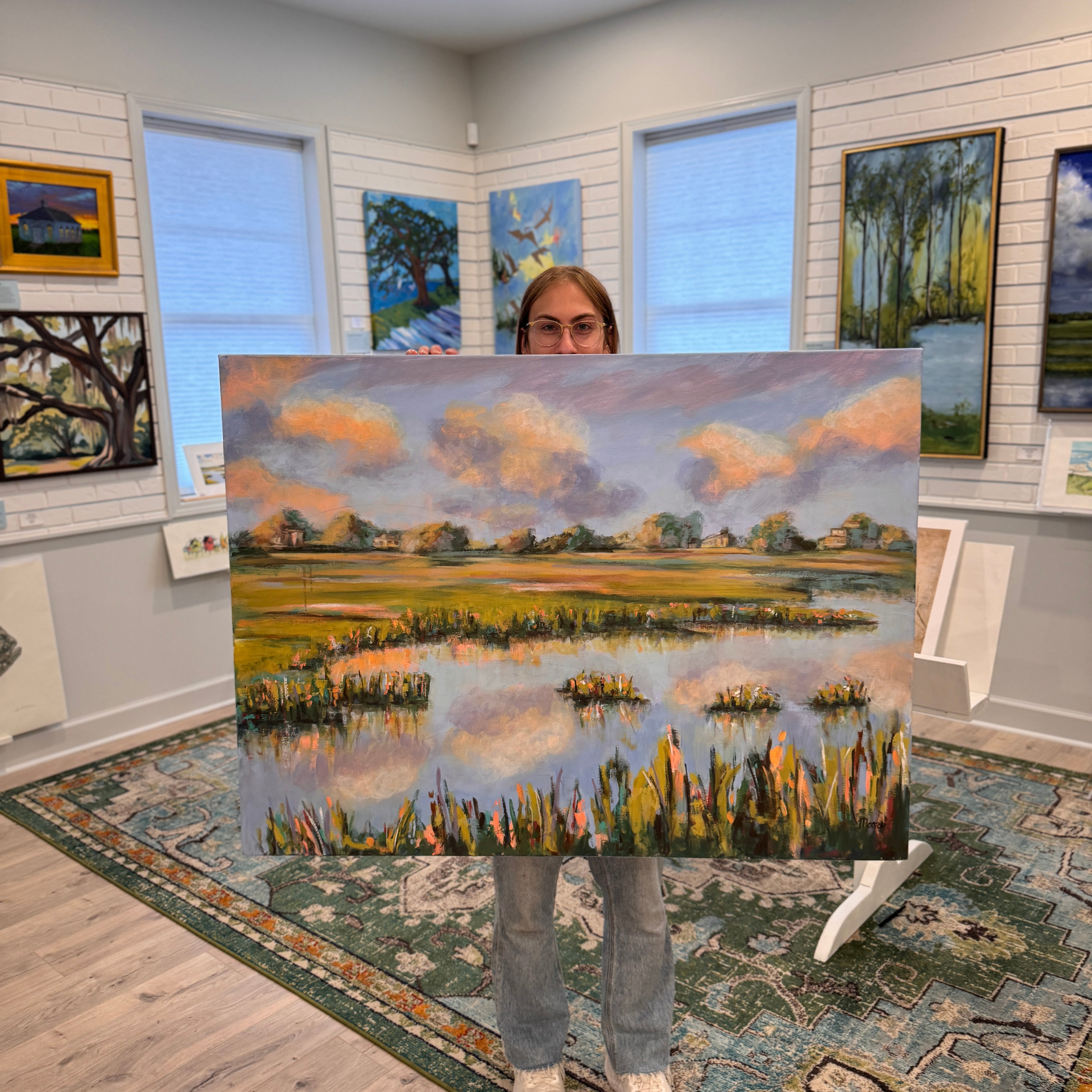 Person holding Golden Hour Reflections, a large 48x36 acrylic marsh painting by Susan Moore, showing scale in the gallery.