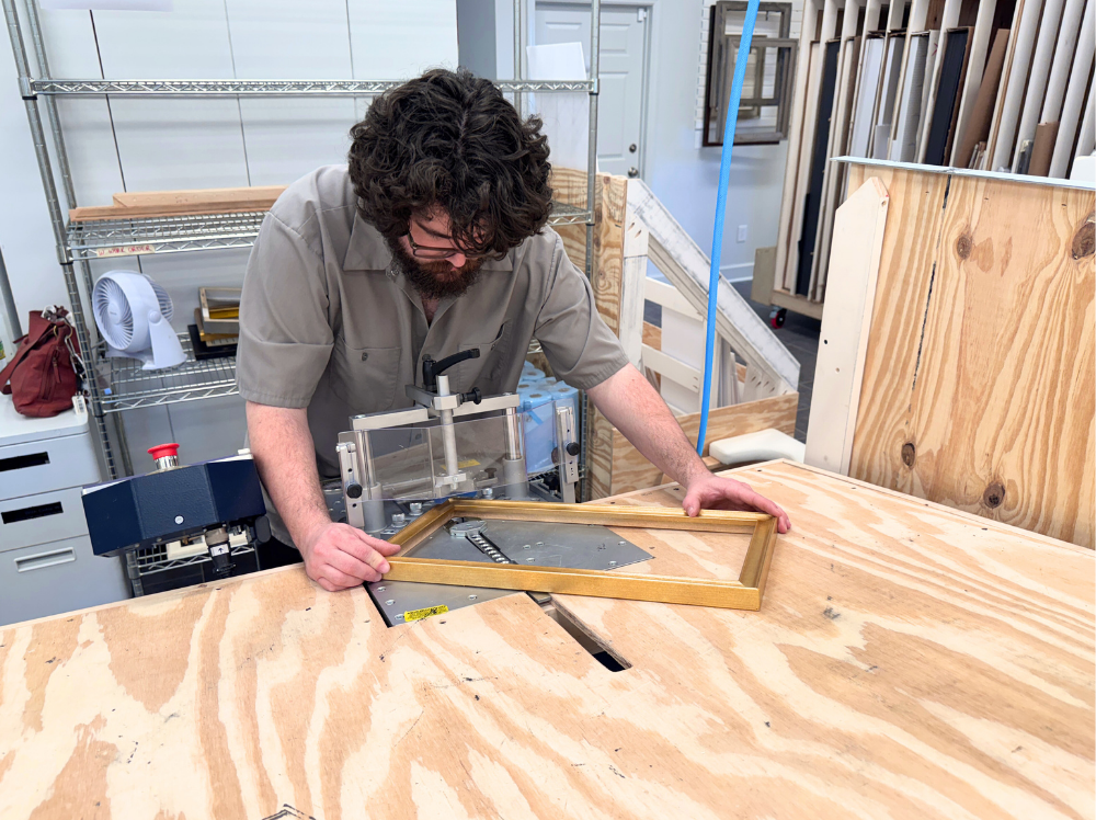 A framer at Gray Man Gallery uses specialized equipment to join the corners of a custom-cut gold frame, ensuring a precise and secure fit.