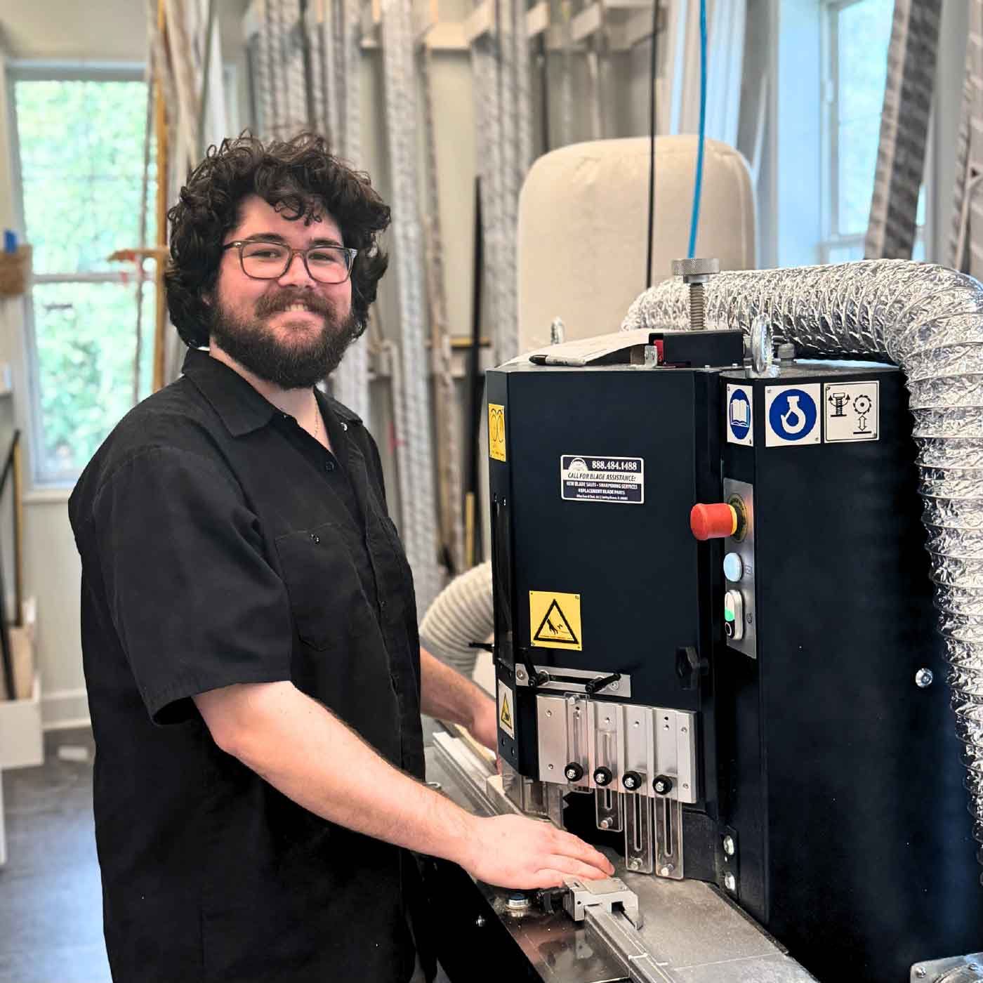 Peyton, a custom framer at Gray Man Gallery, smiles beside professional framing equipment in the workshop.
