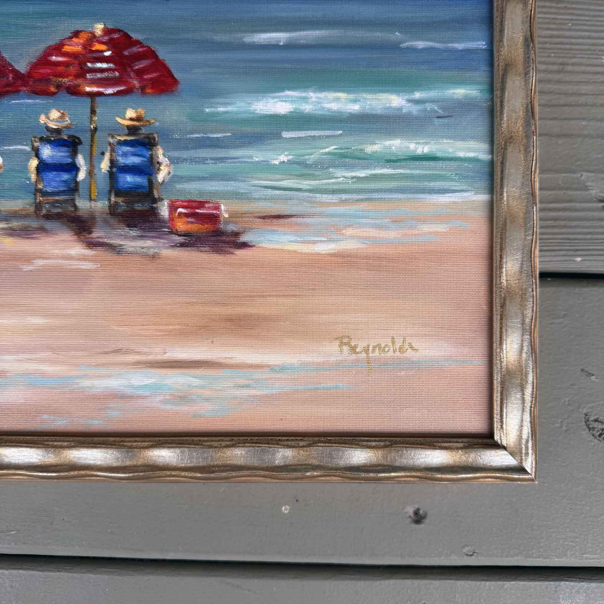 Framed oil painting “The Boardroom” by Jenny Reynolds featuring red beach umbrellas and blue chairs along the shoreline with ocean waves and clouds.