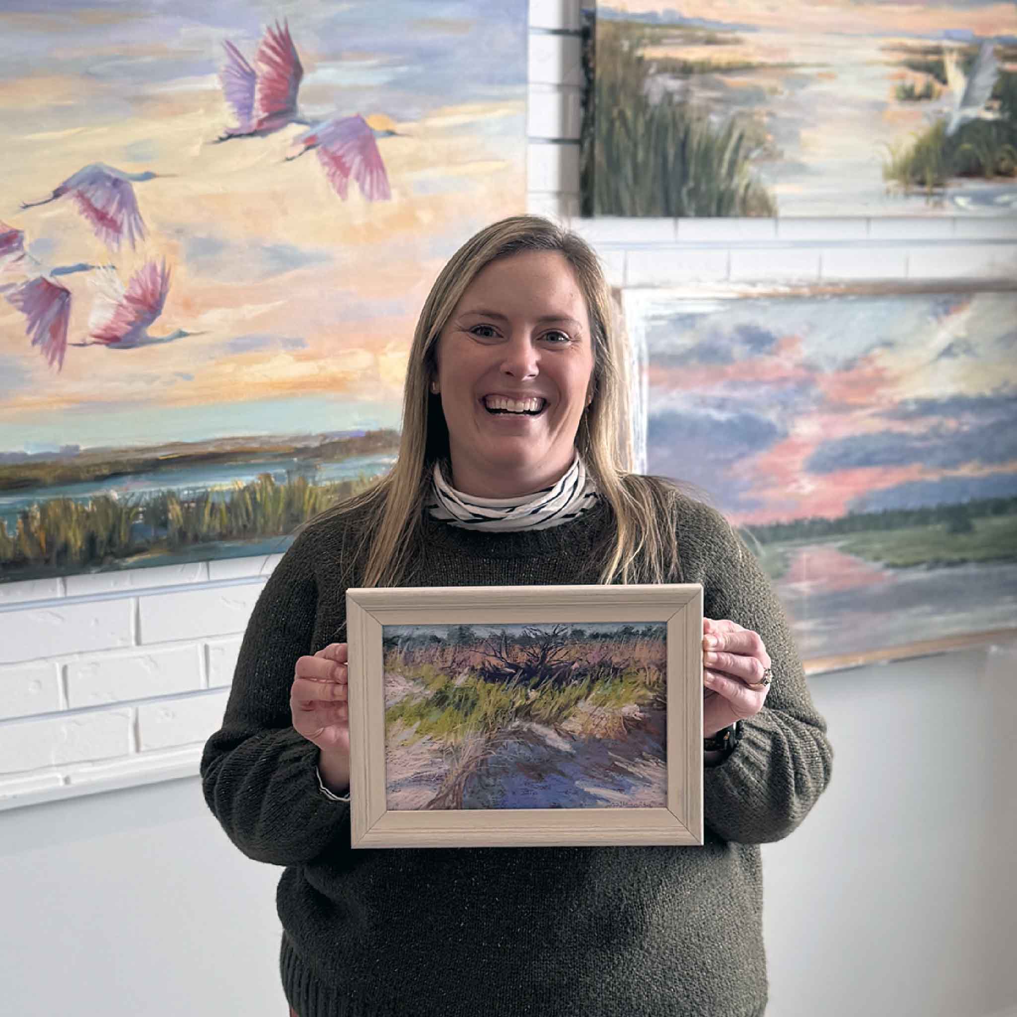 Gray Man Gallery team member Bordy holding framed pastel artwork “A Closer Look” by Joanne Willoughby inside the Pawleys Island gallery, showcasing scale and coastal Lowcountry art