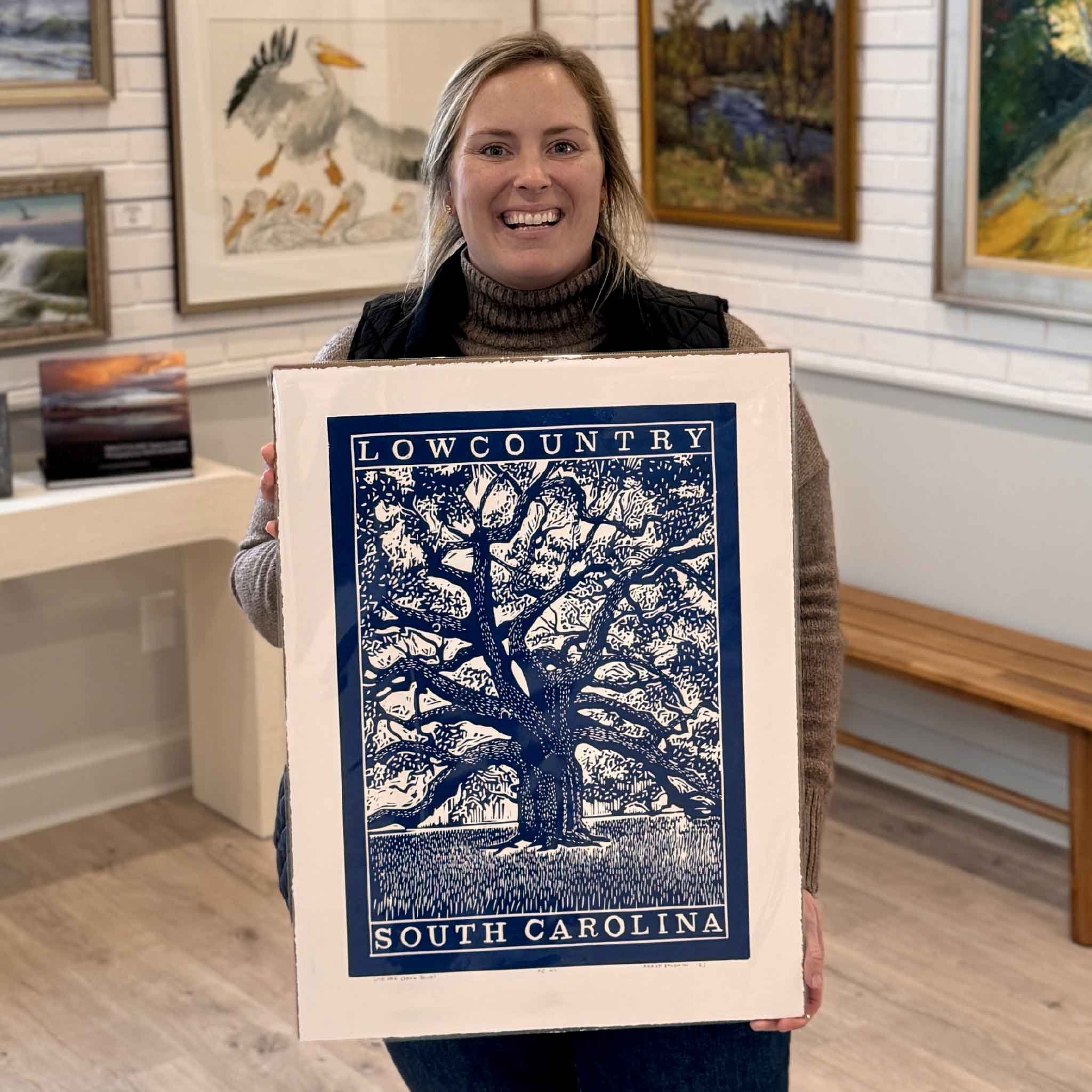 Local artist Aaron Baldwin hand-pulled linocut print titled “Live Oak,” featuring a majestic South Carolina live oak with sweeping branches and dense canopy. Shown as a lifestyle image held at Gray Man Gallery in Pawleys Island, this bold Lowcountry artwork celebrates Southern heritage, coastal Carolina landscapes, and traditional relief printmaking.