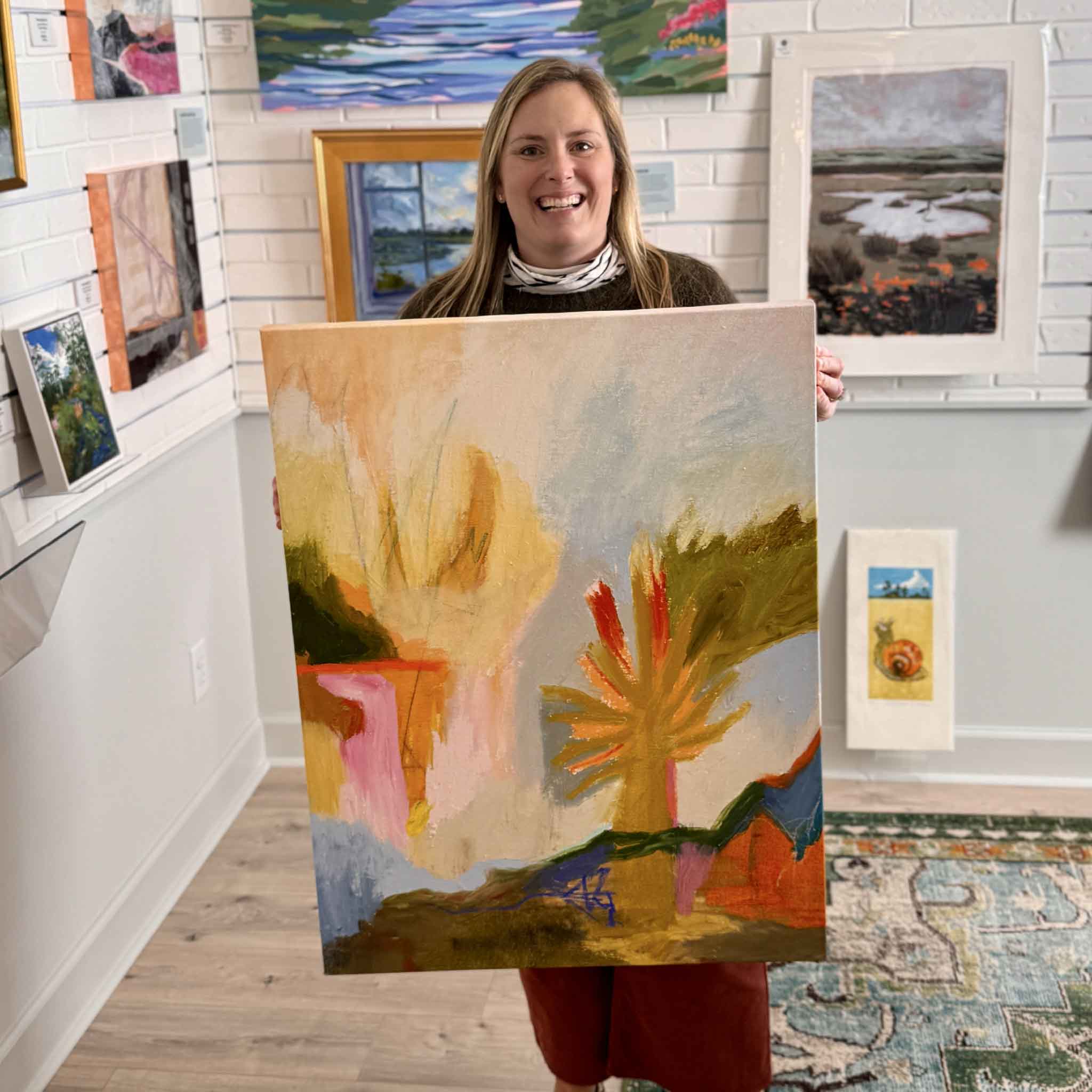 Gray Man Gallery team member Bordy holding Abstract #7 by Caroline Young, a large original abstract painting with yellow, coral, and blue tones, photographed inside the Pawleys Island art gallery to show scale and detail