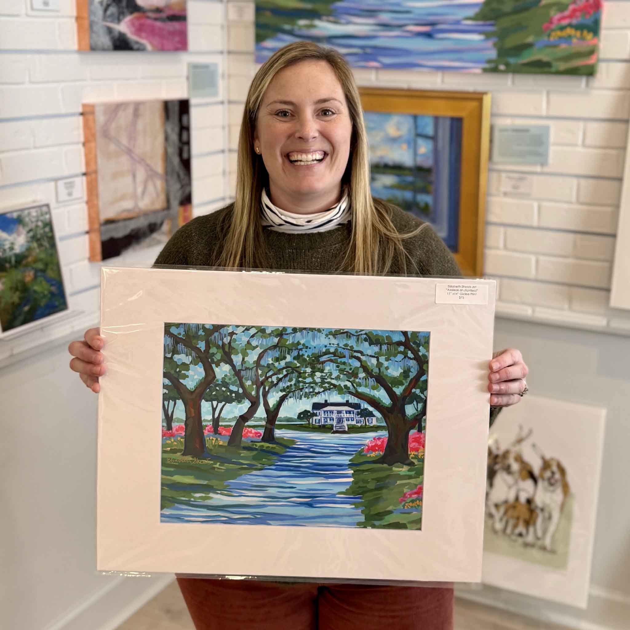 Elizabeth Sheats Azaleas at Litchfield 16x20 matted fine art giclée print held by staff inside Gray Man Gallery in Pawleys Island South Carolina, showcasing Litchfield Plantation entrance with live oaks, Spanish moss, blooming azaleas, and iconic Lowcountry Southern coastal artwork