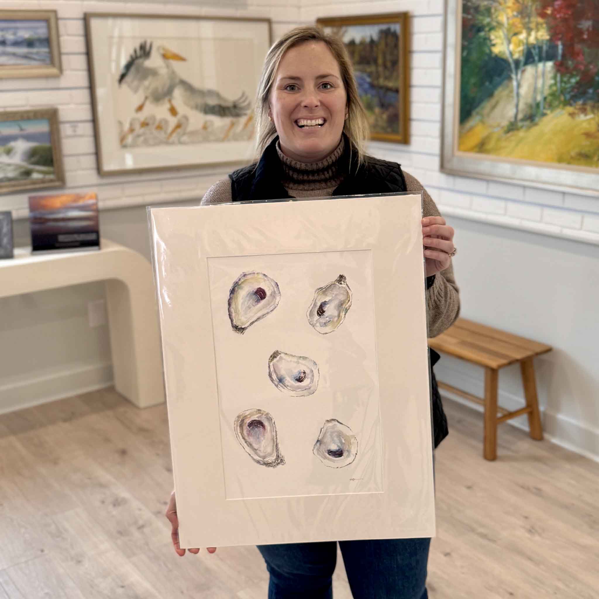Bordy at Gray Man Gallery in Pawleys Island holding Tranquility, an original watercolor by local artist Allison Farr featuring five oyster shells in soft indigo and gray tones, matted to 18x24 and ready for framing