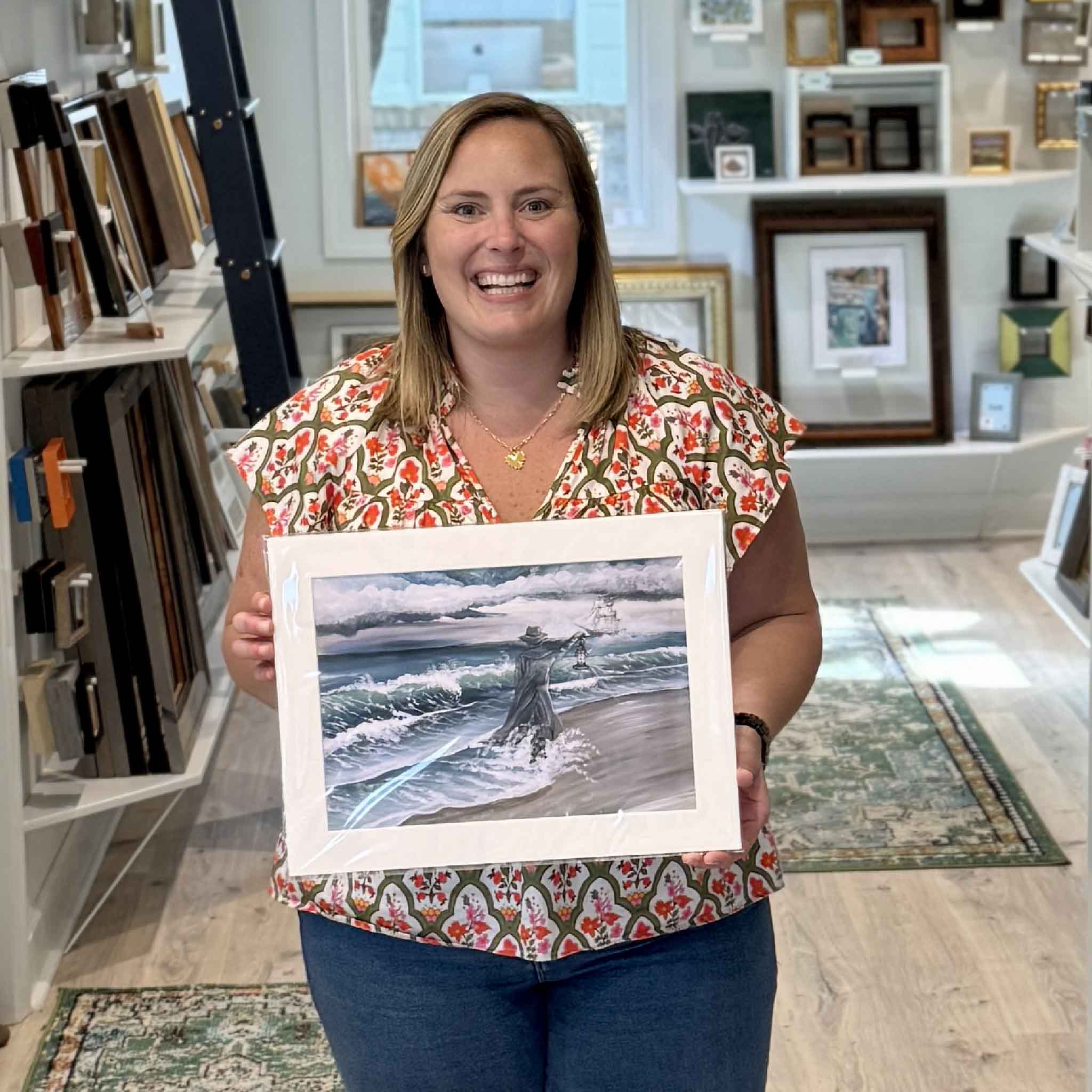 Bordy holding April Bensch Gray Man at Pawleys Island print matted to a standard 12x16 size inside Gray Man Gallery, showing scale of the Lowcountry coastal artwork featuring the Pawleys Island legend