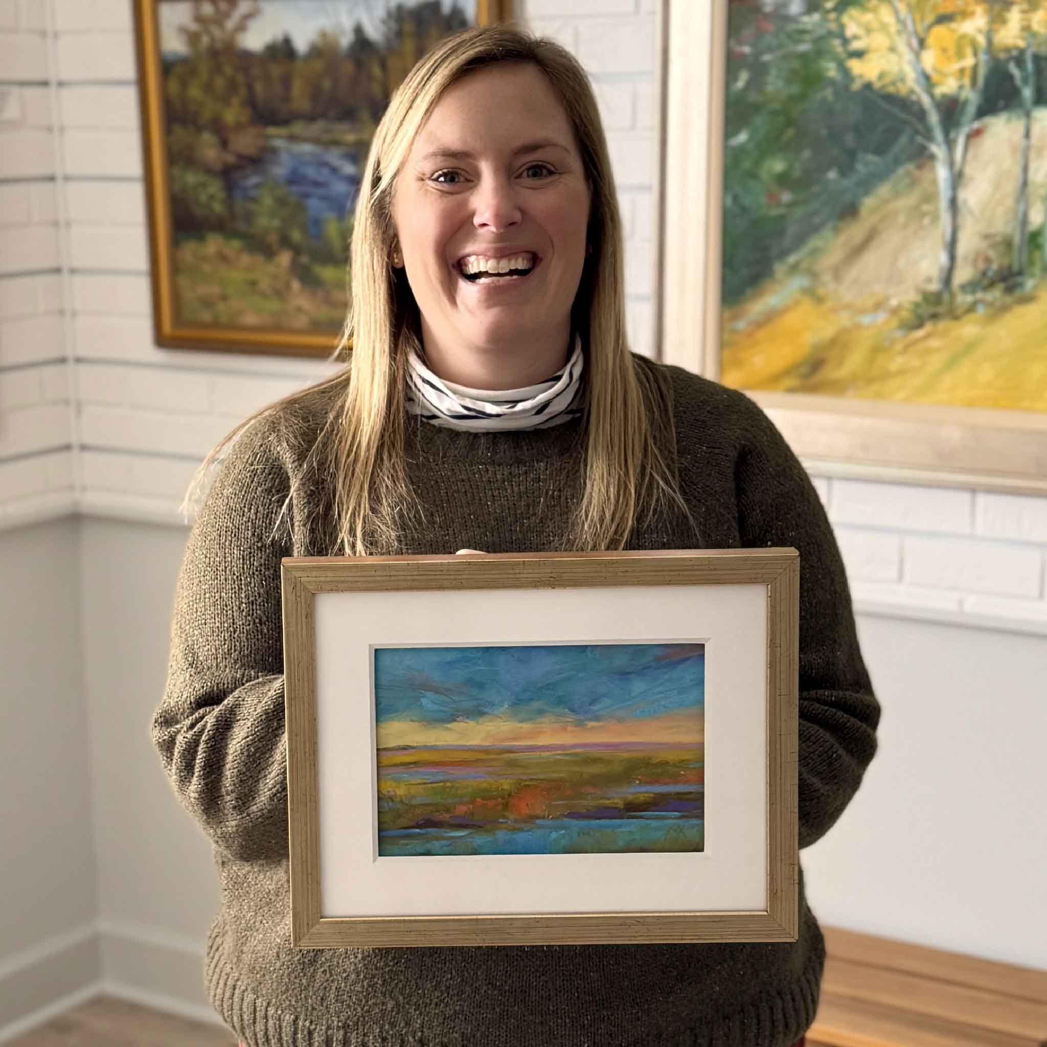 Gray Man Gallery team member Bordy holding “Evening Glow,” an original pastel painting by local Lowcountry artist Vida Miller inside Gray Man Gallery in Pawleys Island, South Carolina, showcasing professionally matted and custom framed coastal landscape artwork