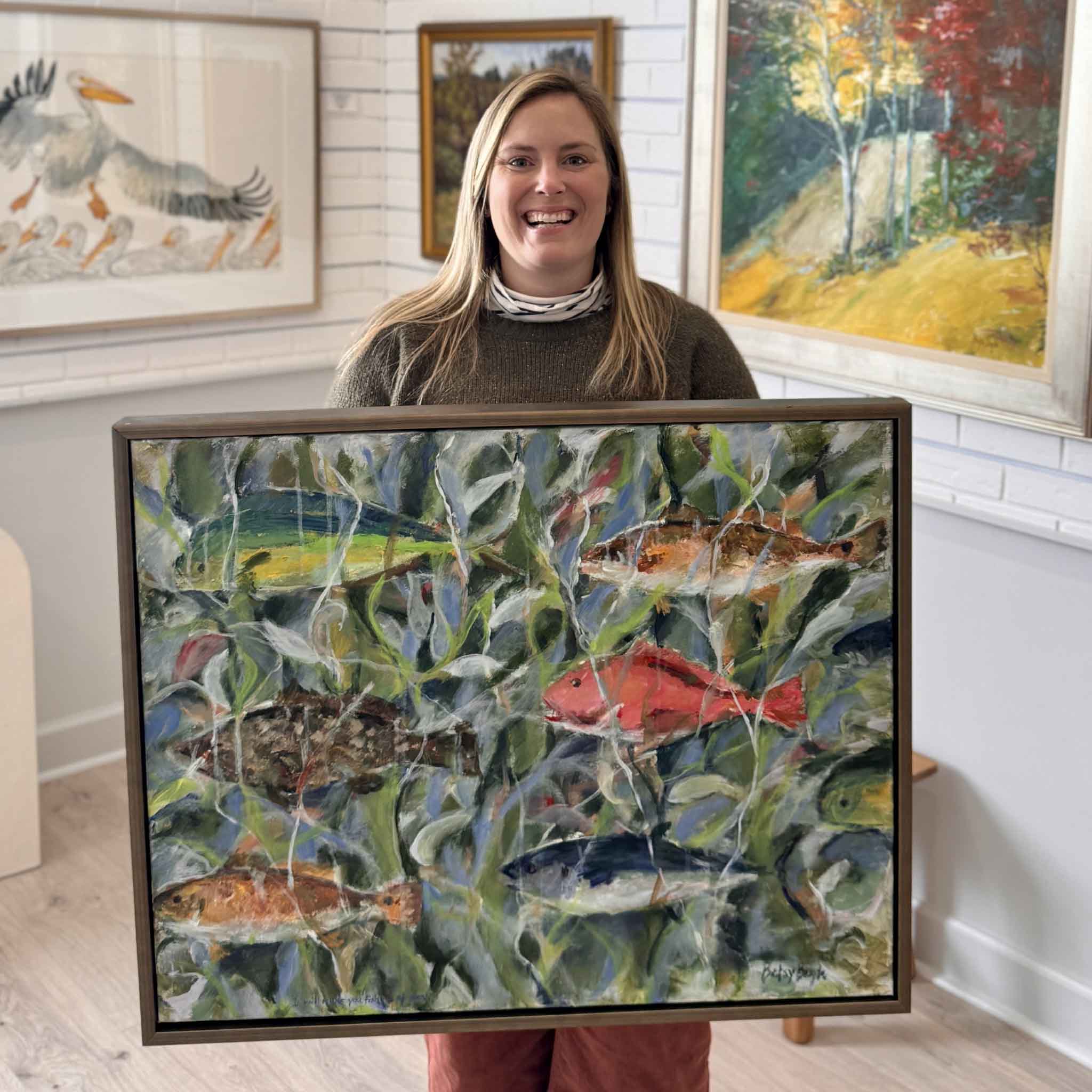 Gray Man Gallery staff member Bordy holding “Fishers of Men,” an original custom framed painting by local Lowcountry artist Betsy Boyle at Gray Man Gallery in Pawleys Island, South Carolina, featuring coastal marsh fish imagery, contemporary coastal art, and expert custom framing