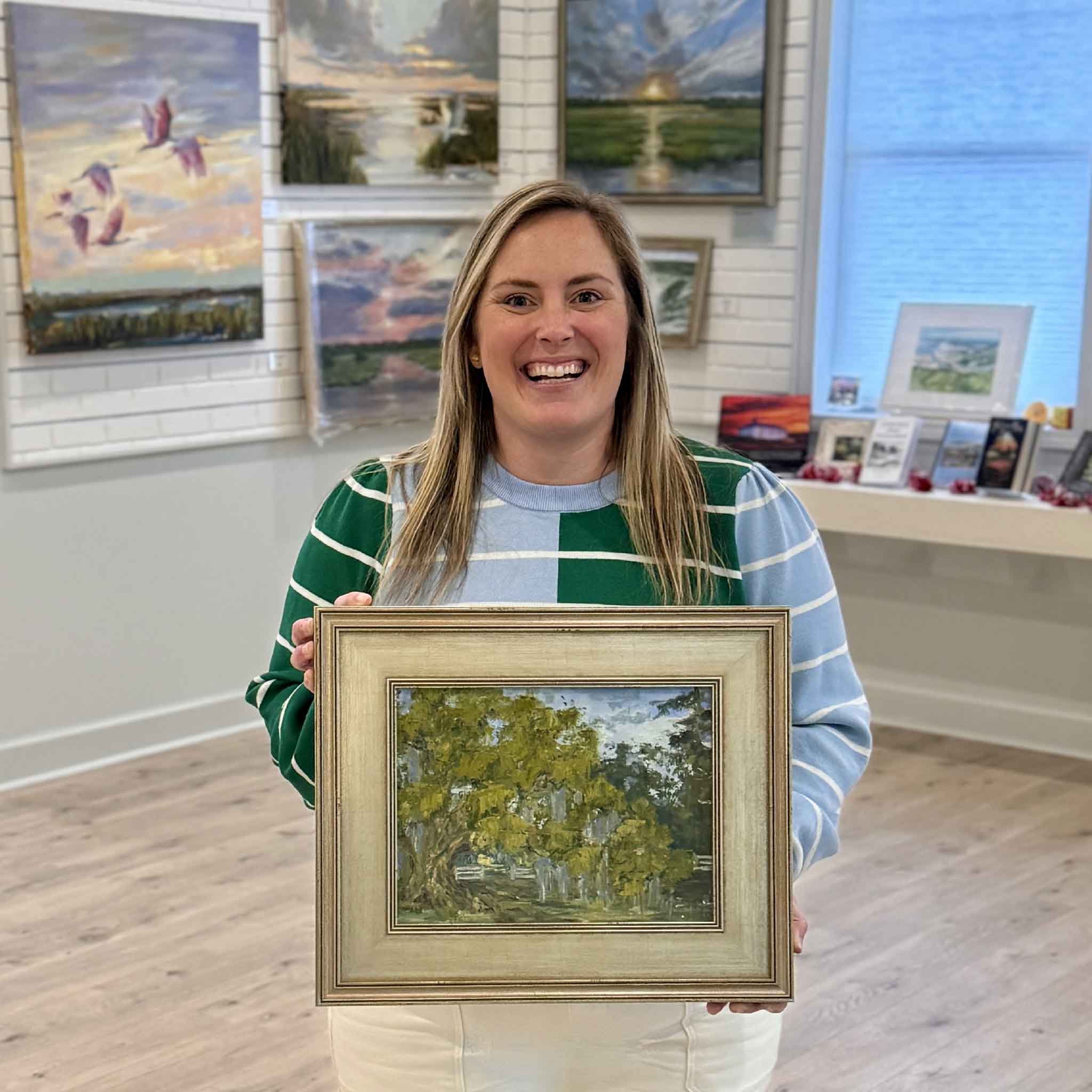 Bordy of Gray Man Gallery standing inside the Pawleys Island gallery holding “Lower Waverly,” an original oil painting by Jeanne O’Neal depicting a moss-draped oak and historic Lowcountry landscape in Georgetown County South Carolina, showcasing scale, framing craftsmanship, and curated Southern art environment
