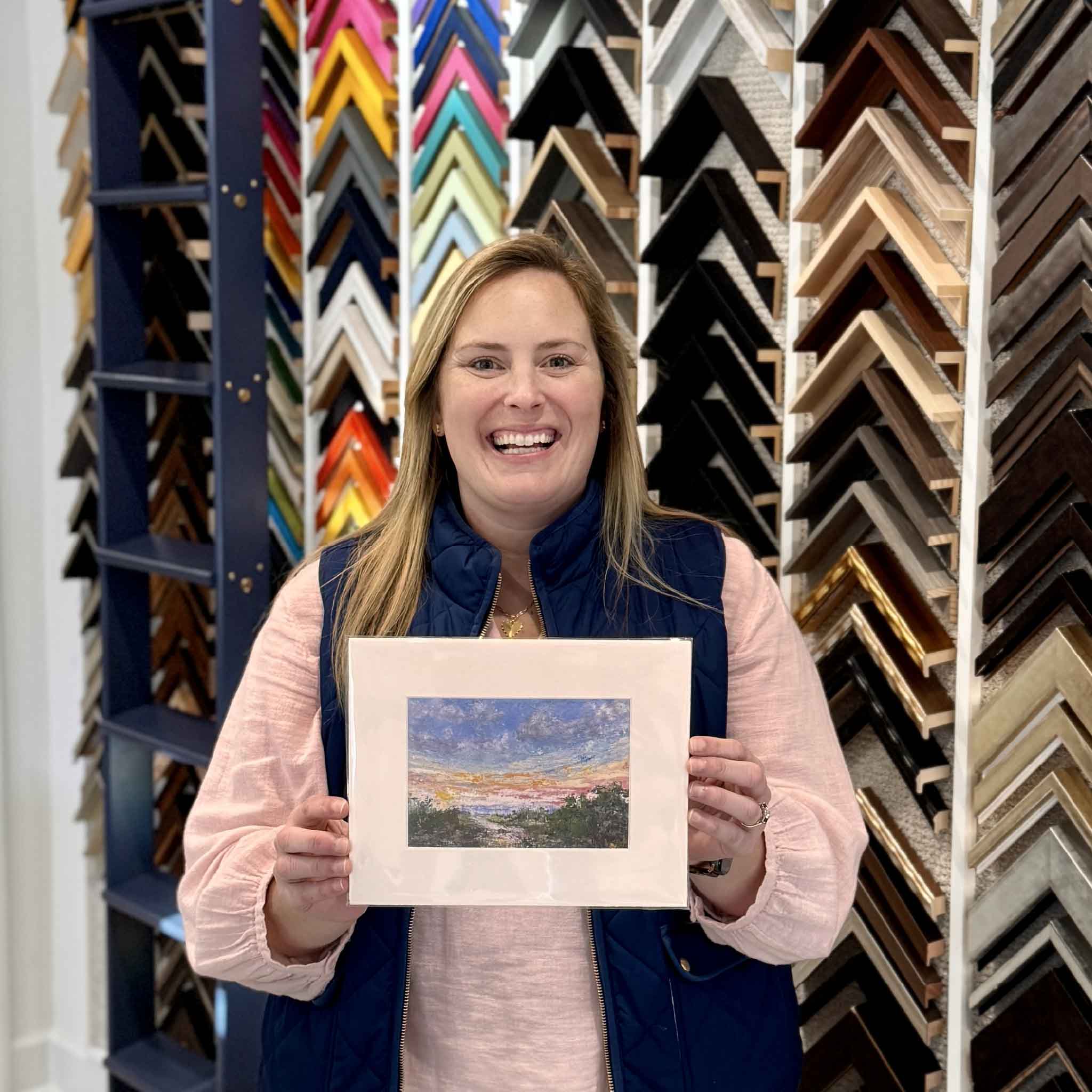 Bordy holding the 8x10 matted fine art giclée print of Marshlight by local Pawleys Island artist Jeanne O’Neal inside Gray Man Gallery, highlighting the vibrant Lowcountry marsh sunset scene reproduced with archival inks and designed to fit standard 8x10 frames