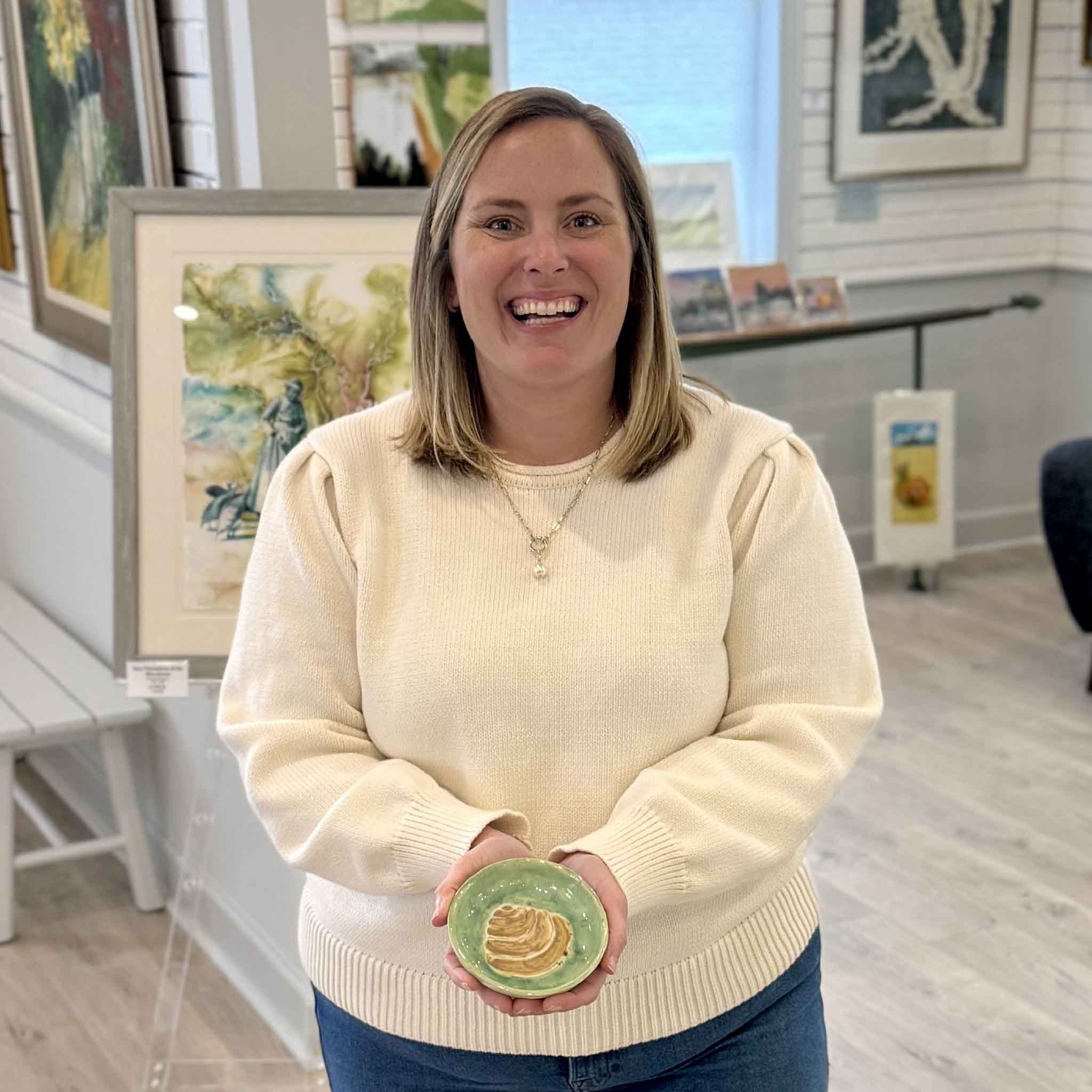 Bordy holding a handmade green Pawleys Island shell dish by local artist Vida Miller inside Gray Man Gallery showing scale and detail of the ceramic piece