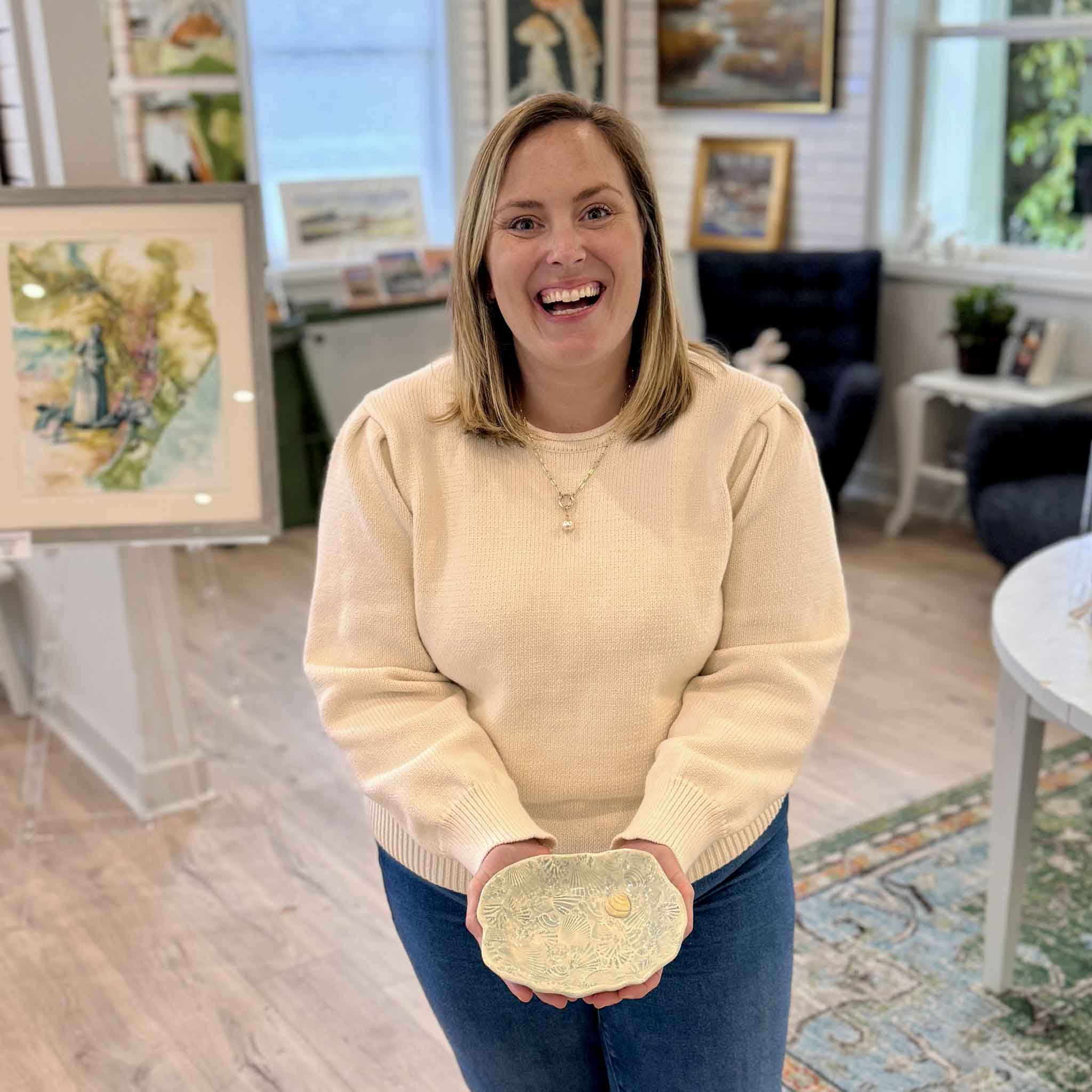 Bordy holding Pawleys Shore Shell Dish in Coastal Wash by local artist Vida Miller inside Gray Man Gallery showing scale of the ceramic dish with shell textures