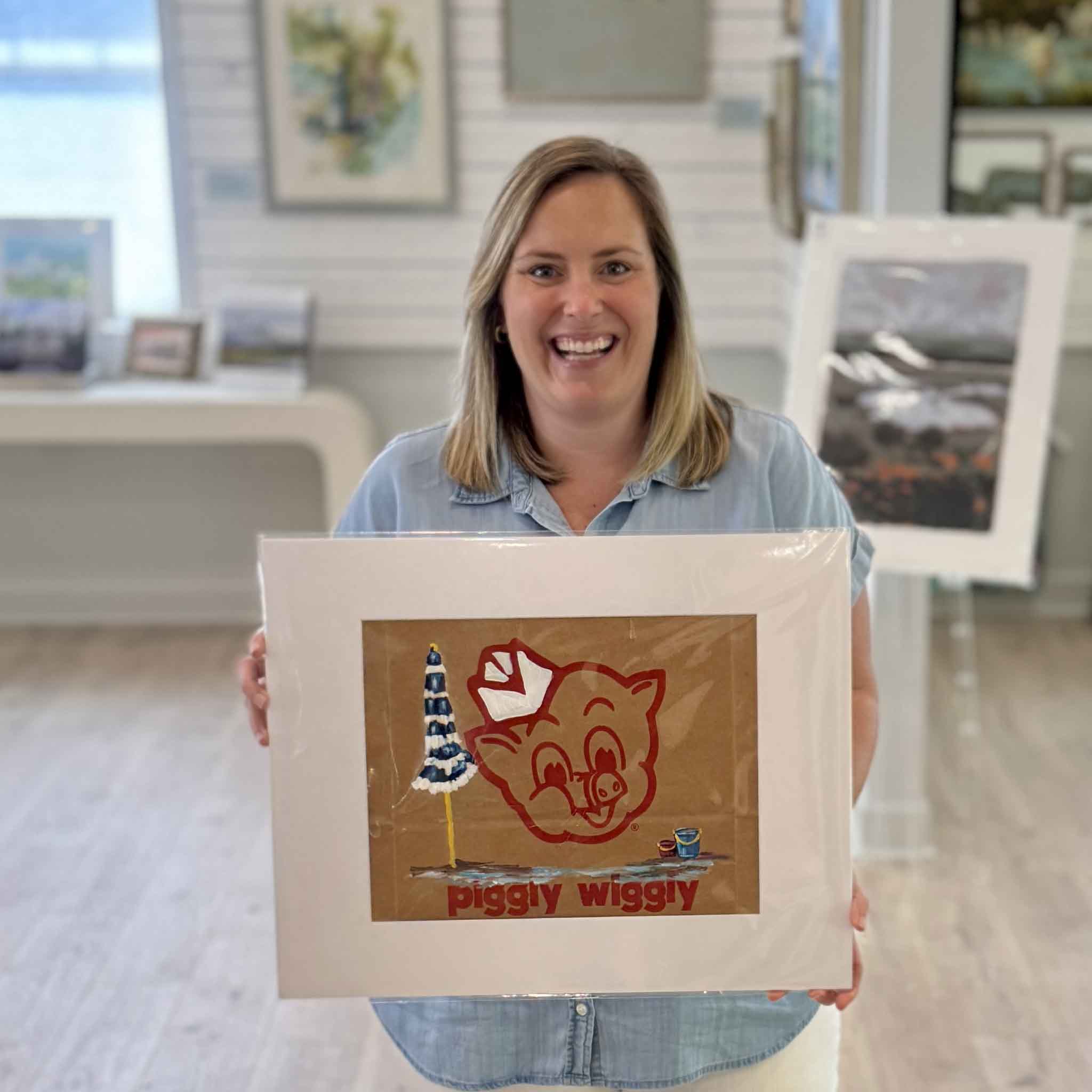 Bordy at Gray Man Gallery holding Piggly Wiggly Beach Day painting by local artist Jenny Reynolds on an authentic grocery bag, showing size and detail of the artwork