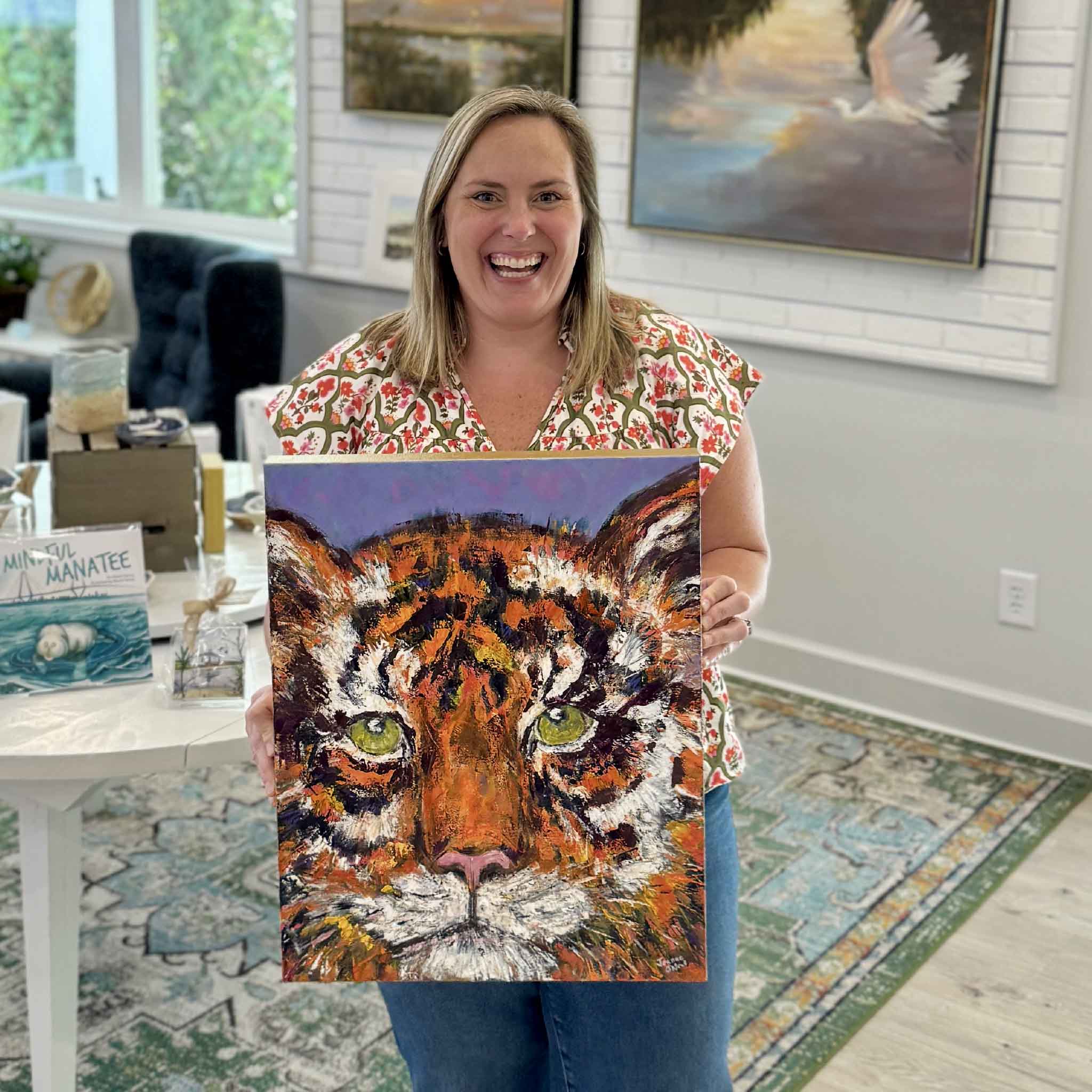 Bordy holds Roar, an original gallery-wrapped tiger oil painting by local artist Jeanne O’Neal at Gray Man Gallery in Pawleys Island, South Carolina. The expressive contemporary artwork features an intense tiger portrait with vivid Clemson-inspired orange tones, heavy texture, and luminous green eyes.