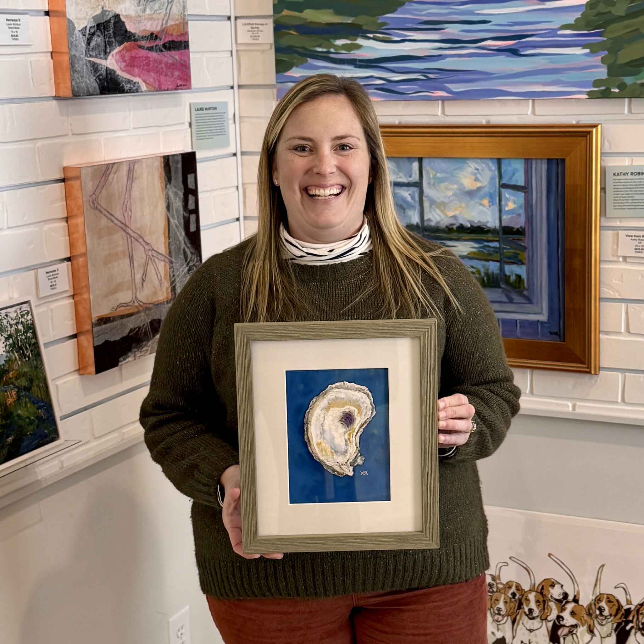 Gray Man Gallery team member Bordy holding Salt Marsh Muse, an original oyster shell watercolor and pastel painting by Pawleys Island artist Vida Miller inside Gray Man Gallery