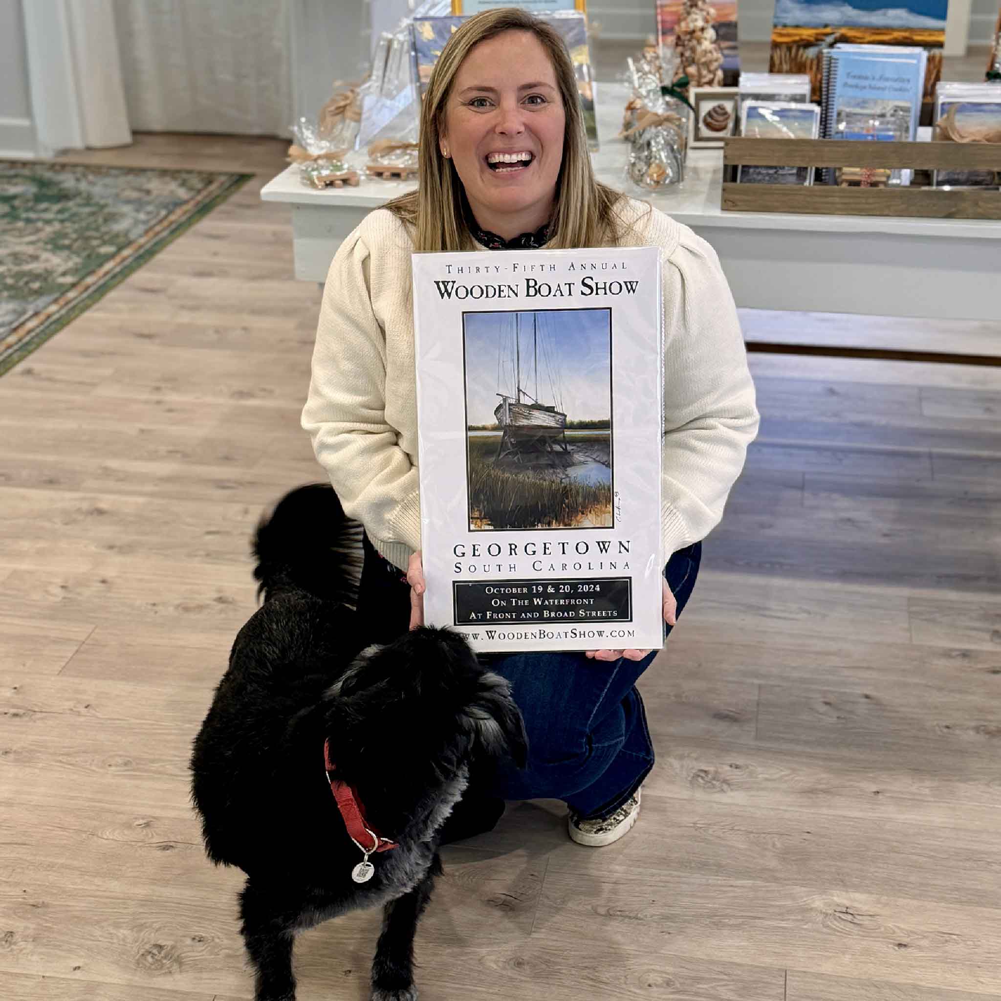 Bordy holding the signed 2024 Georgetown Wooden Boat Show poster by Charles Williams inside Gray Man Gallery in Pawleys Island, South Carolina, showcasing the official collectible 12 x 20 inch event poster.