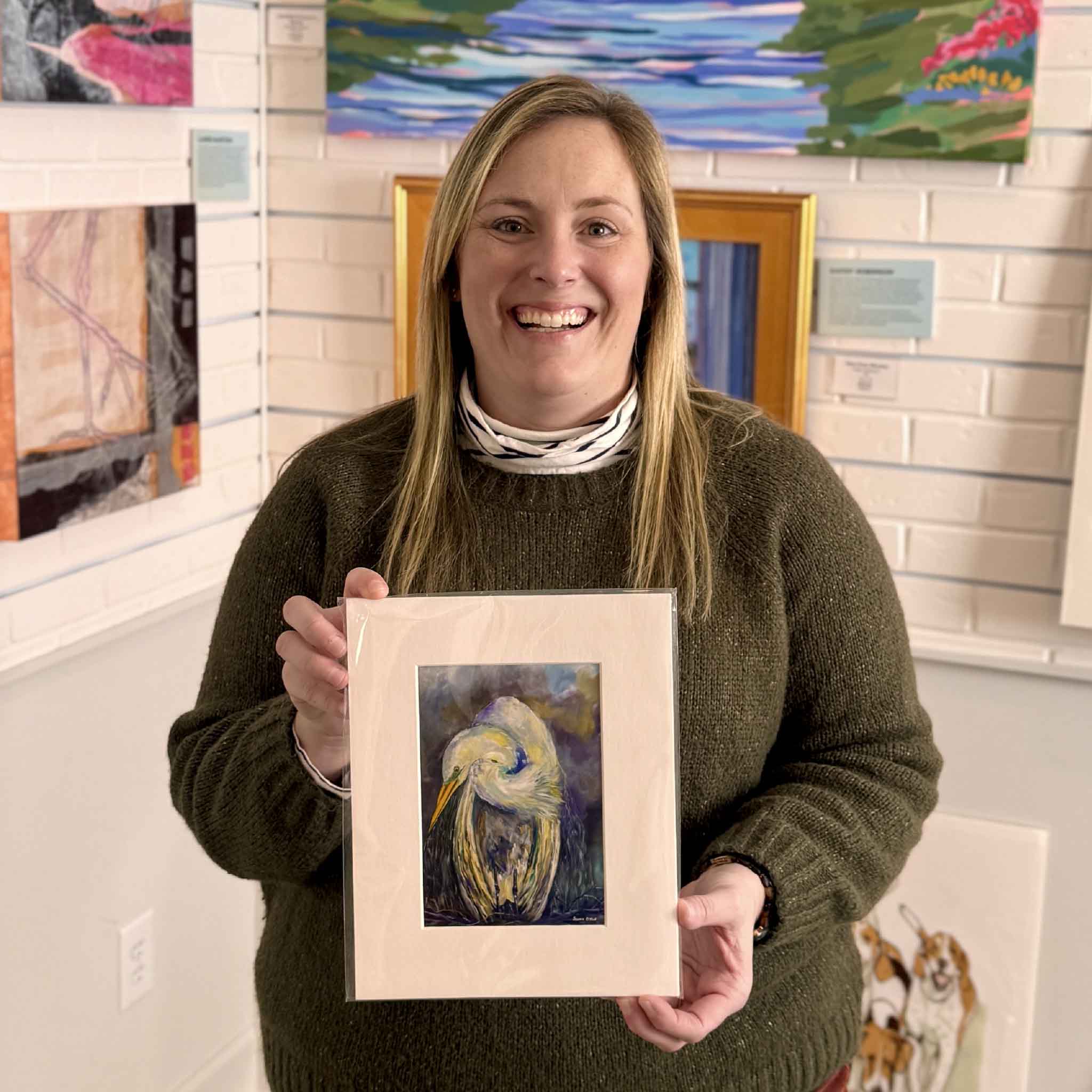 Gray Man Gallery staff member Bordy holding “Strength” by Jeanne O’Neal, a matted great white heron fine art giclée print, inside the Pawleys Island art gallery showcasing local Lowcountry artists