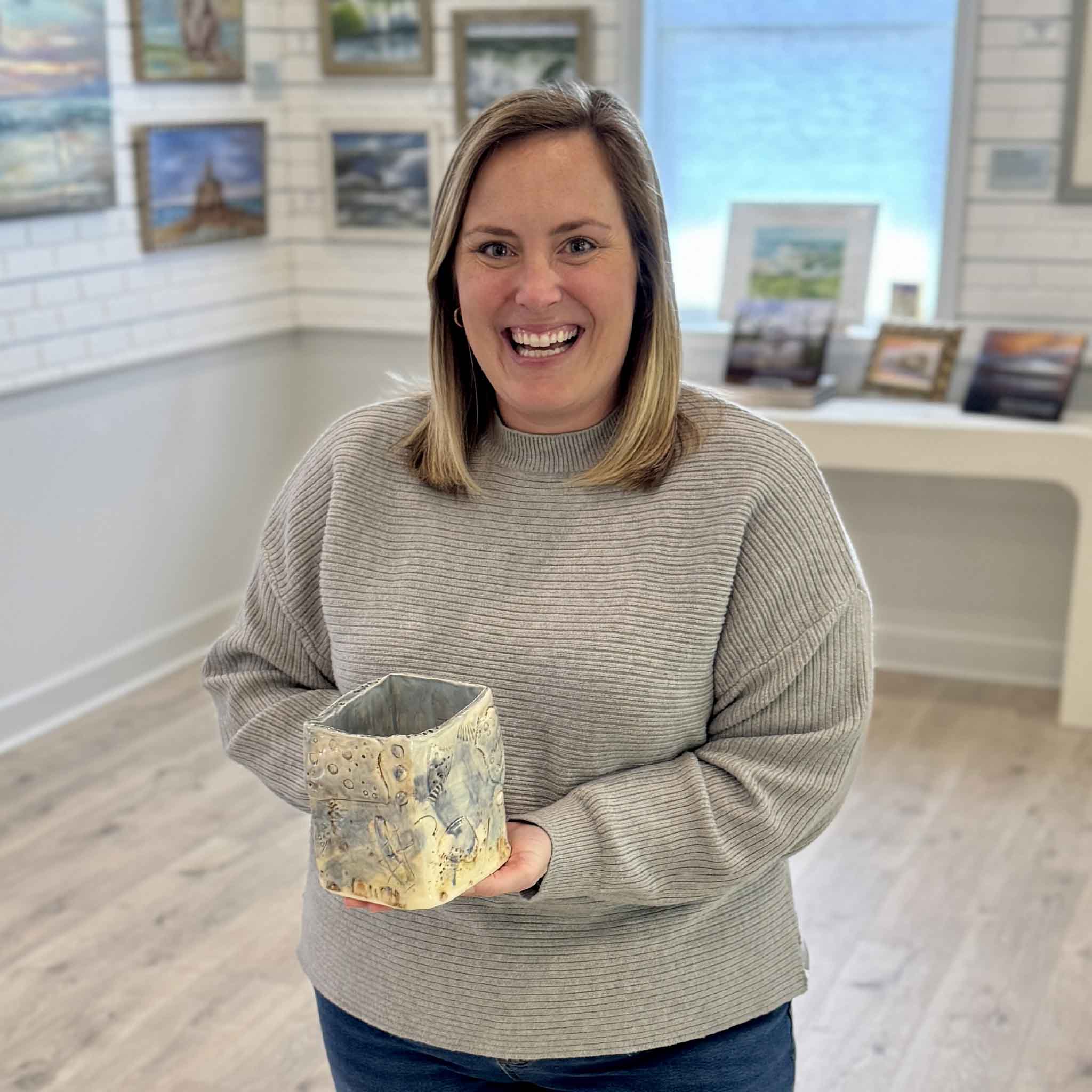 Bordy holding Salt Relic Vessel by Vida Miller inside Gray Man Gallery in Pawleys Island, South Carolina, showing the scale of the handbuilt ceramic vase with coastal-inspired blue and gray glaze, textured surface with shell impressions and organic markings, and a sculptural, irregular form