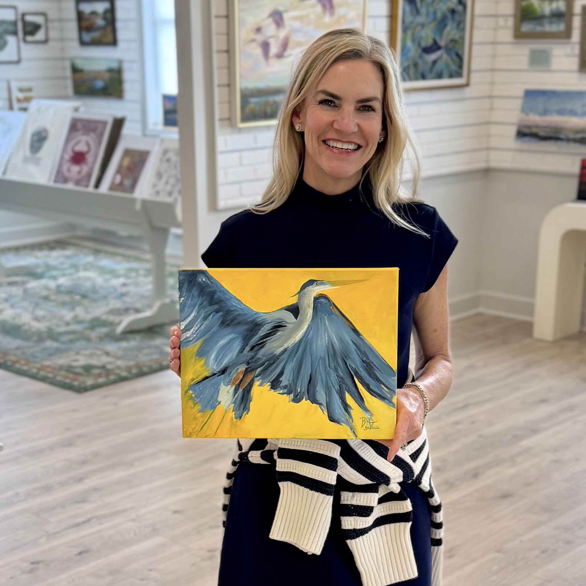 Braden Grafe holding Sunshine original oil painting in Gray Man Gallery in Pawleys Island, featuring a dynamic great blue heron in flight with expressive blue tones and a vibrant yellow background, gallery wrapped coastal artwork by local artist