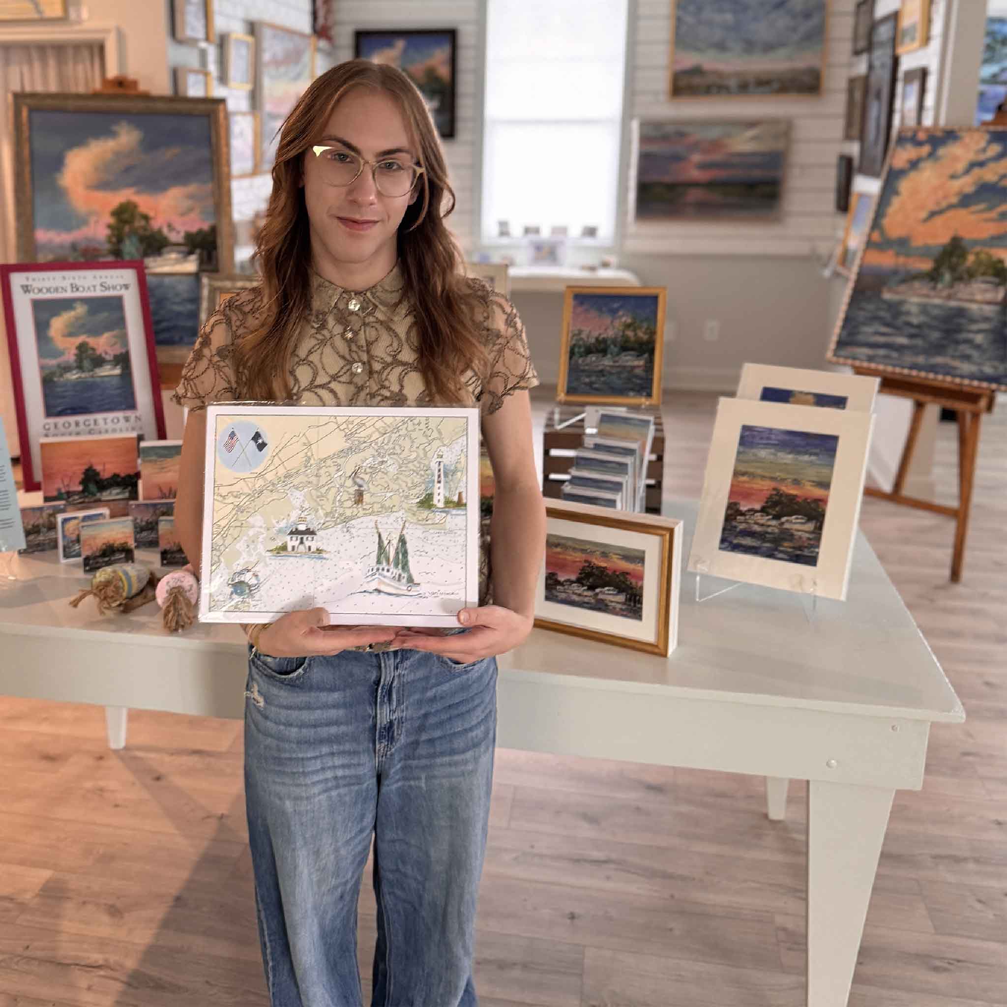 Gray Man Gallery team member holding Bulls Bay Map by Vida Miller, a nautical chart artwork featuring Cape Romain Lighthouse, Bulls Bay, McClellanville shrimp boats, and Lowcountry coastal history.