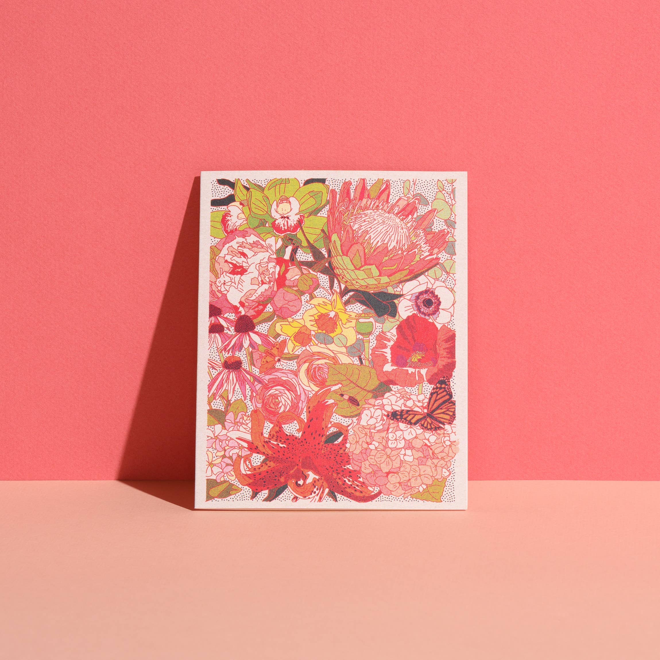 Colorful Wild Florals notecard from the Caroline Clark boxed stationery set, featuring intricate protea, lilies, poppies, hydrangeas, roses, coneflowers and a butterfly in shades of coral, pink, green and yellow, photographed against a bright coral background for Gray Man Gallery in Pawleys Island, South Carolina.