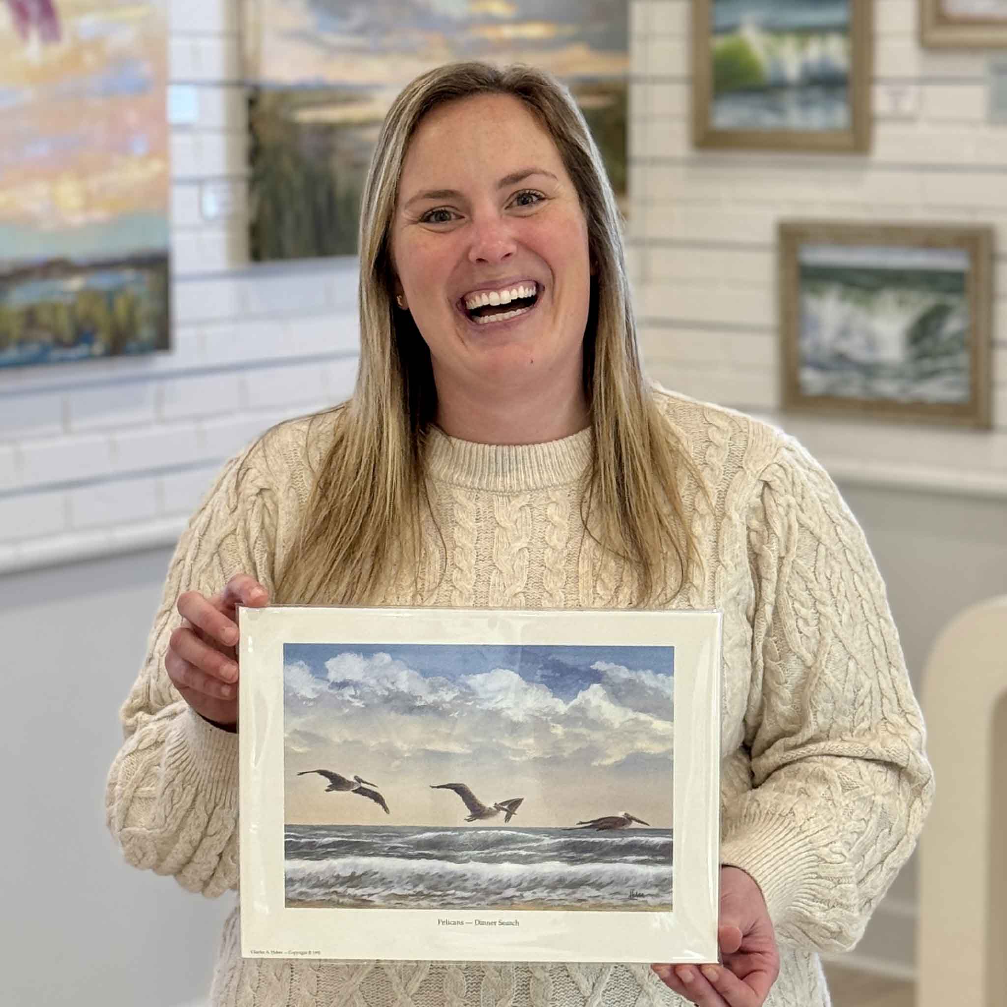Gray Man Gallery staff member Bordy holding Pelicans Dinner Search print by Pawleys Island artist Charles Huber to show scale, featuring pelicans gliding over coastal surf and Lowcountry sky.
