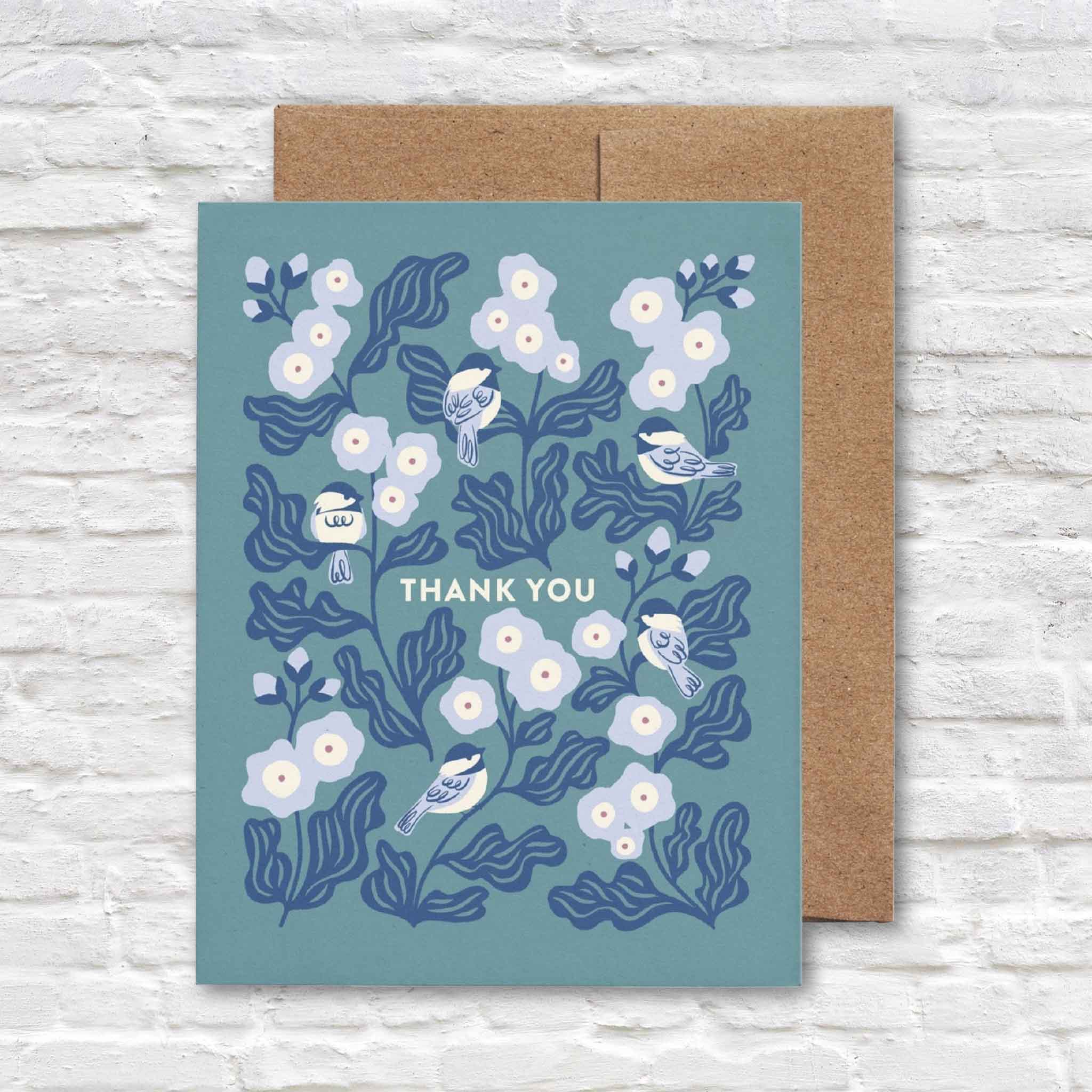 Chickadee Thank You greeting card by Chrissie Van Hoever featuring delicate chickadees perched among blooming hollyhock flowers on a blue background with a recycled kraft envelope. Sustainably printed and available at Gray Man Gallery in Pawleys Island, South Carolina.
