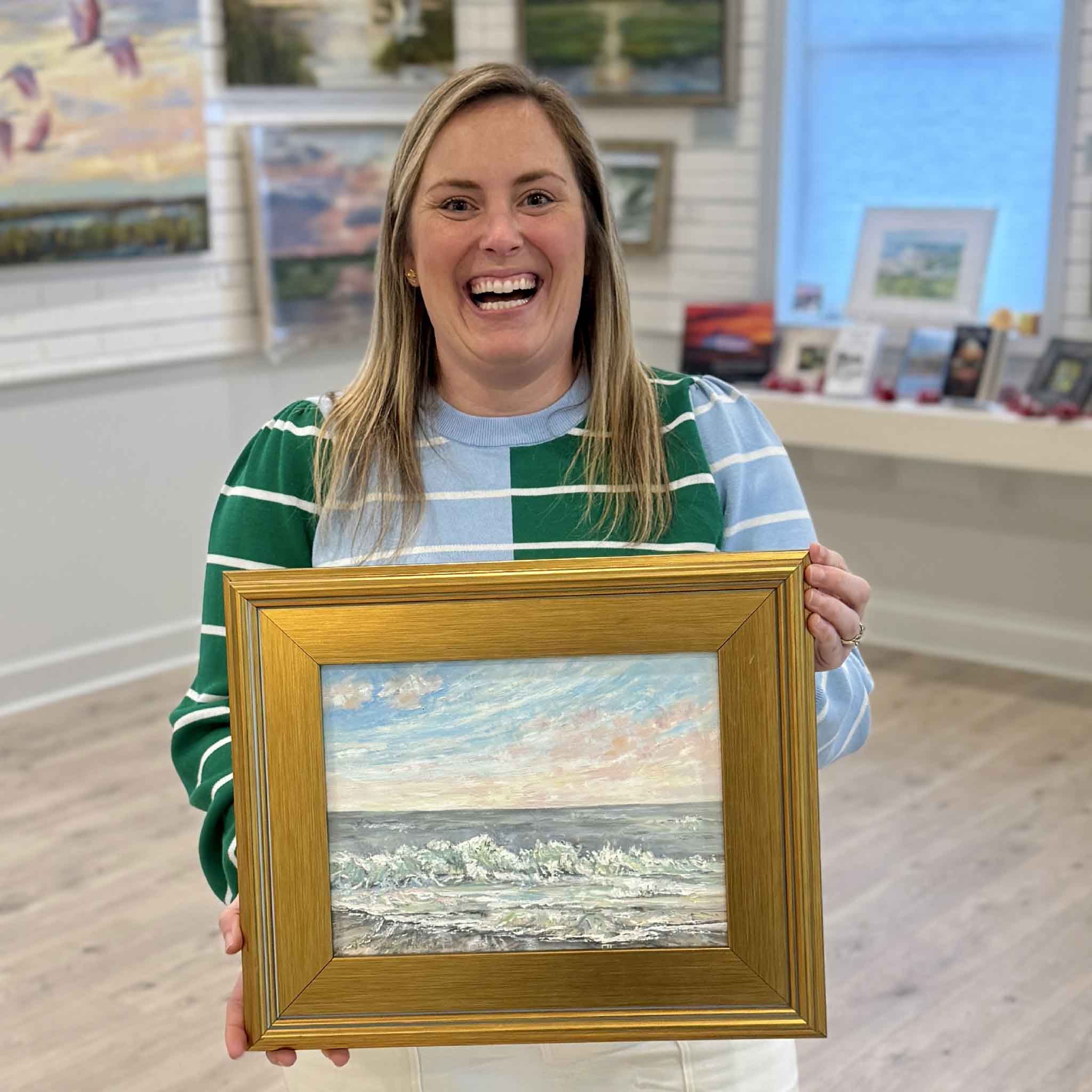 Bordy holding Coastal Calm original oil painting by Jeanne O’Neal inside Gray Man Gallery in Pawleys Island, showcasing framed coastal artwork inspired by the South Carolina shoreline