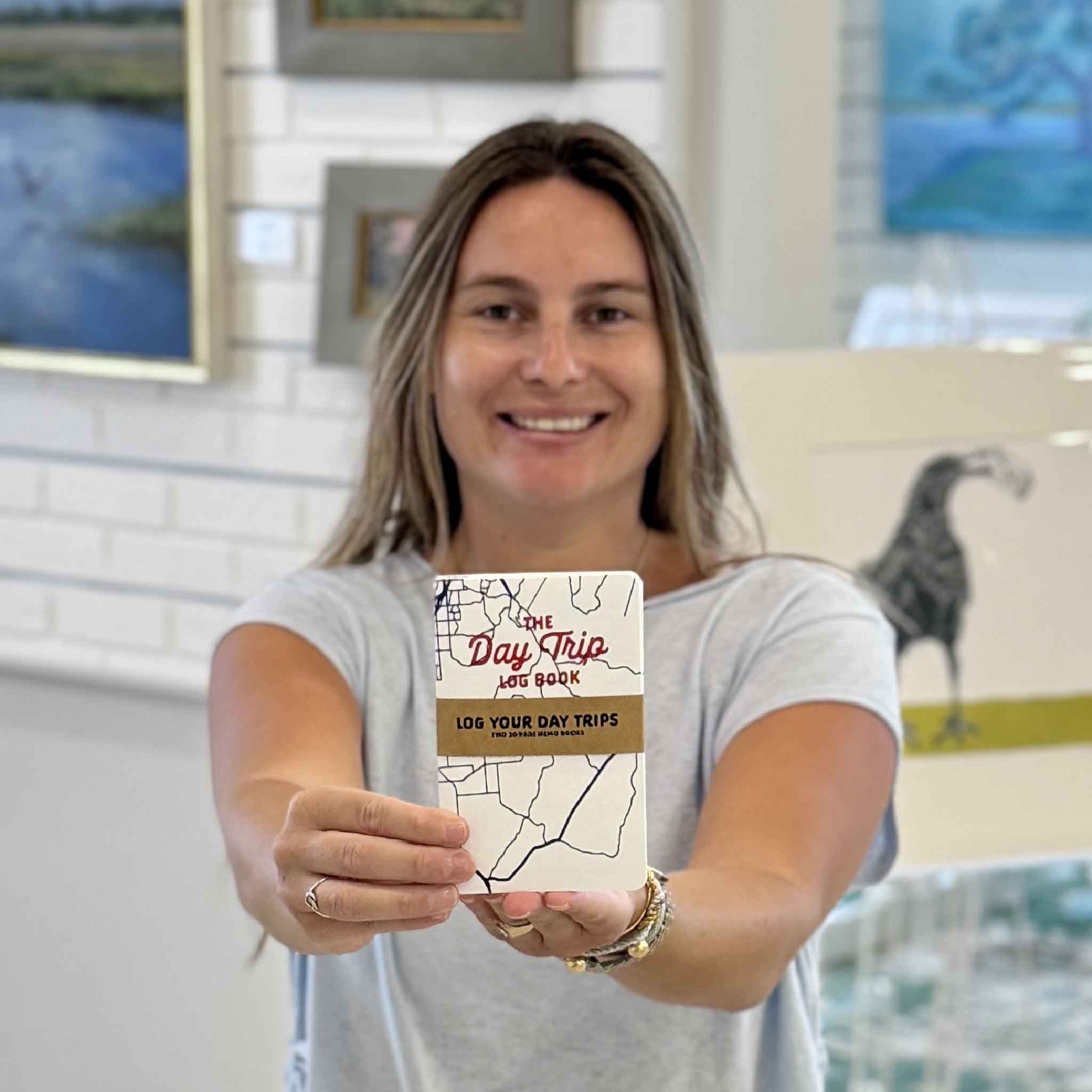 The Day Trip Log Book available at Gray Man Gallery in Pawleys Island, South Carolina, shown in hand. Pocket-sized travel journal for tracking road trips, day trips, destinations, travel memories, and favorite places to revisit.